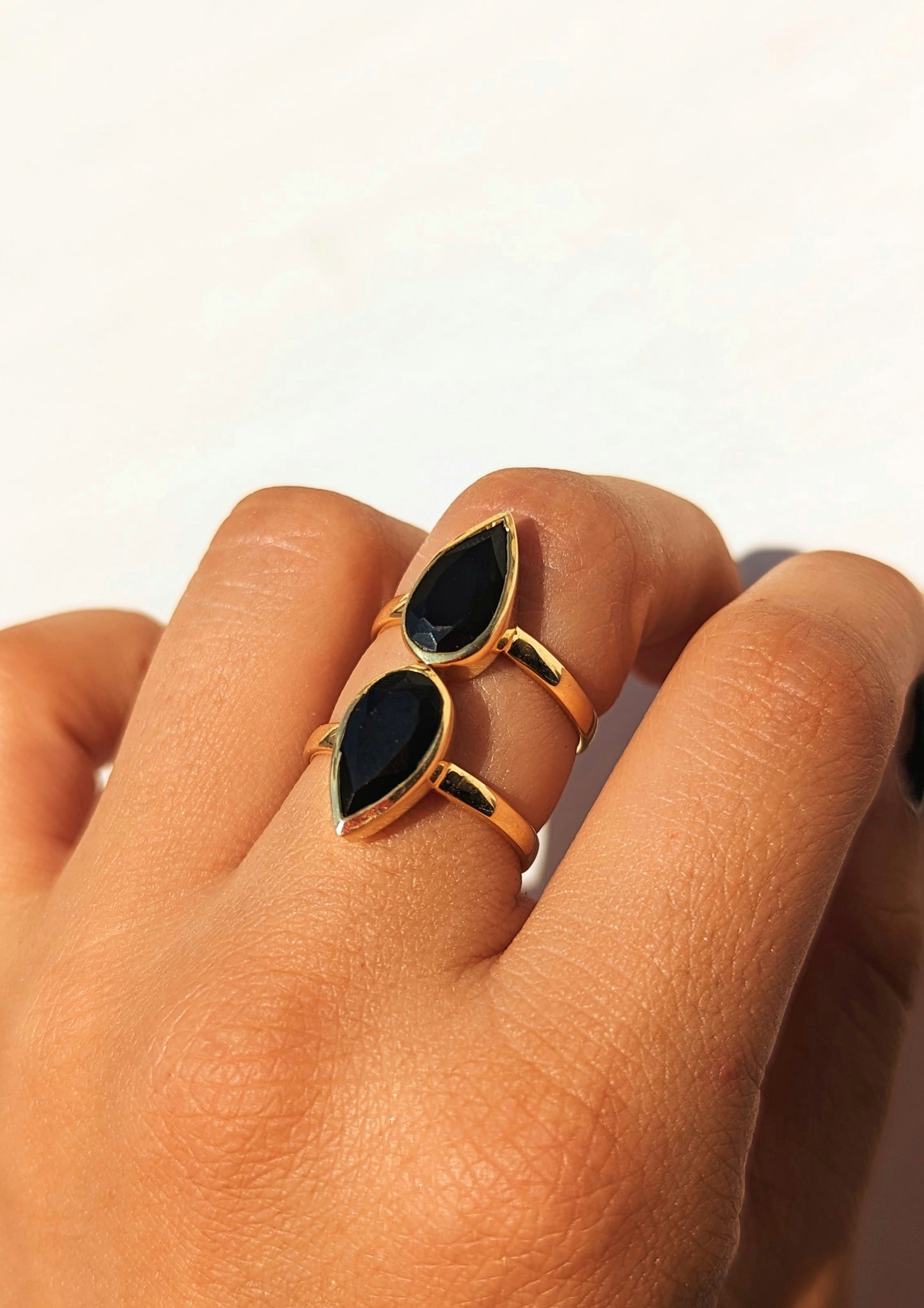 Hand wearing a gold ring with two teardrop-shaped black onyx stones, paired with a delicate gold circle necklace from Moon & Milk.