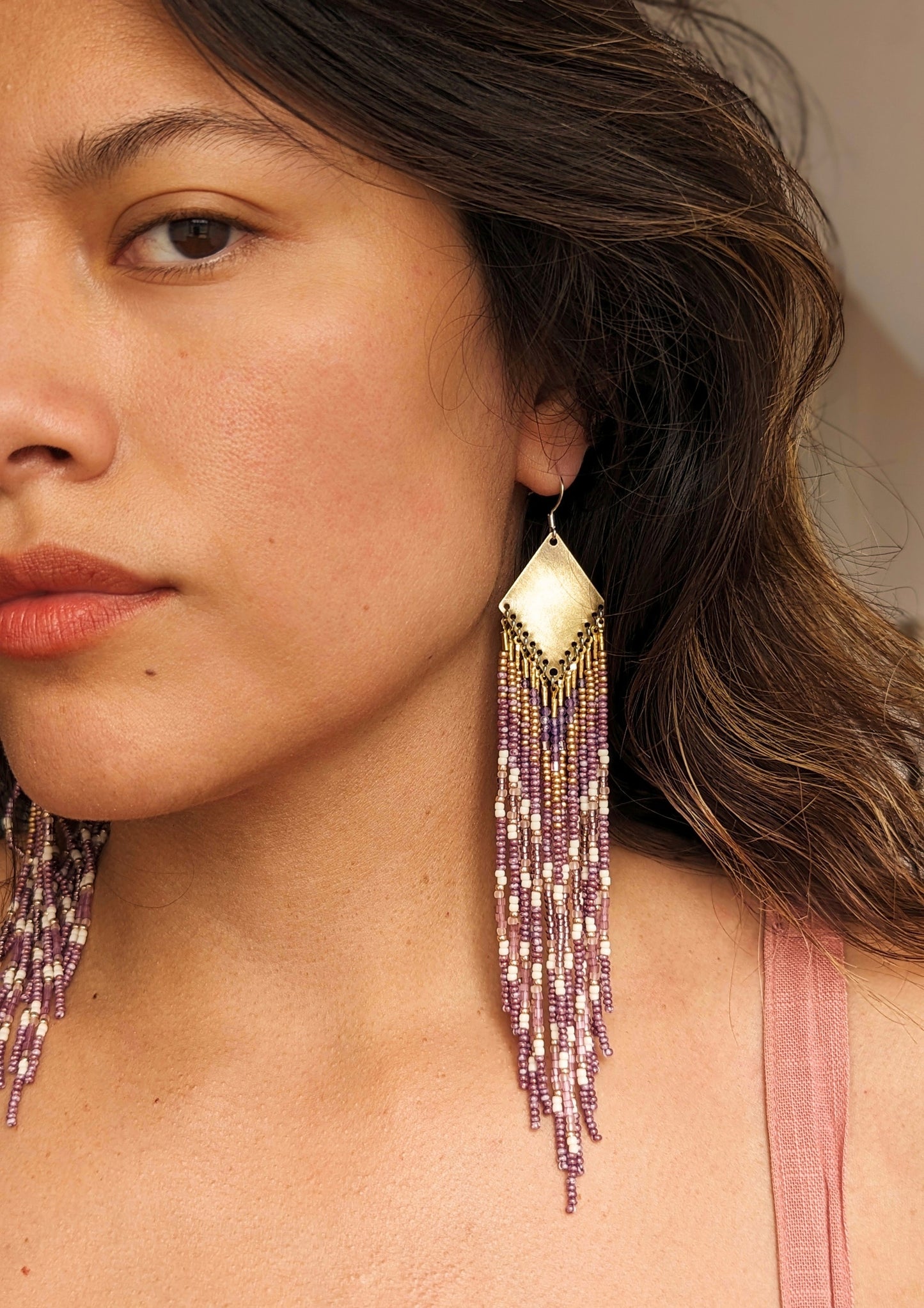 Moon & Milk long beaded earrings in gold, lavender, and cream tones, handcrafted with glass beads and brass worn by a woman.
