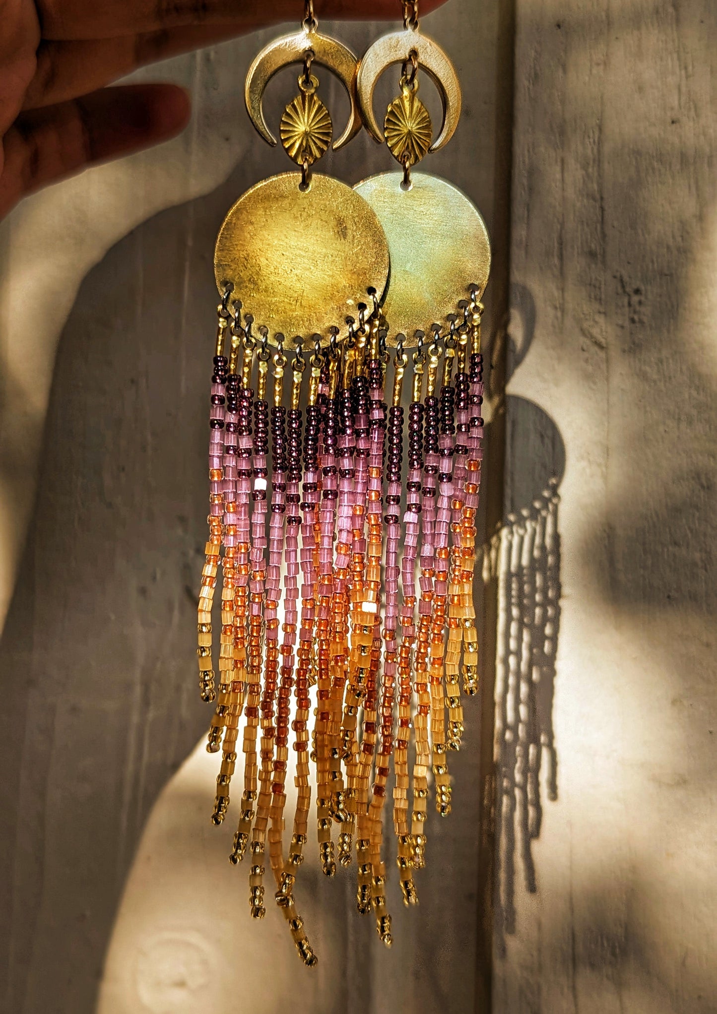 Moon & Milk earrings inspired by La Quebrada, featuring sunset-toned beadwork in gold, amber, and amethyst with brass moons and circular medallions.