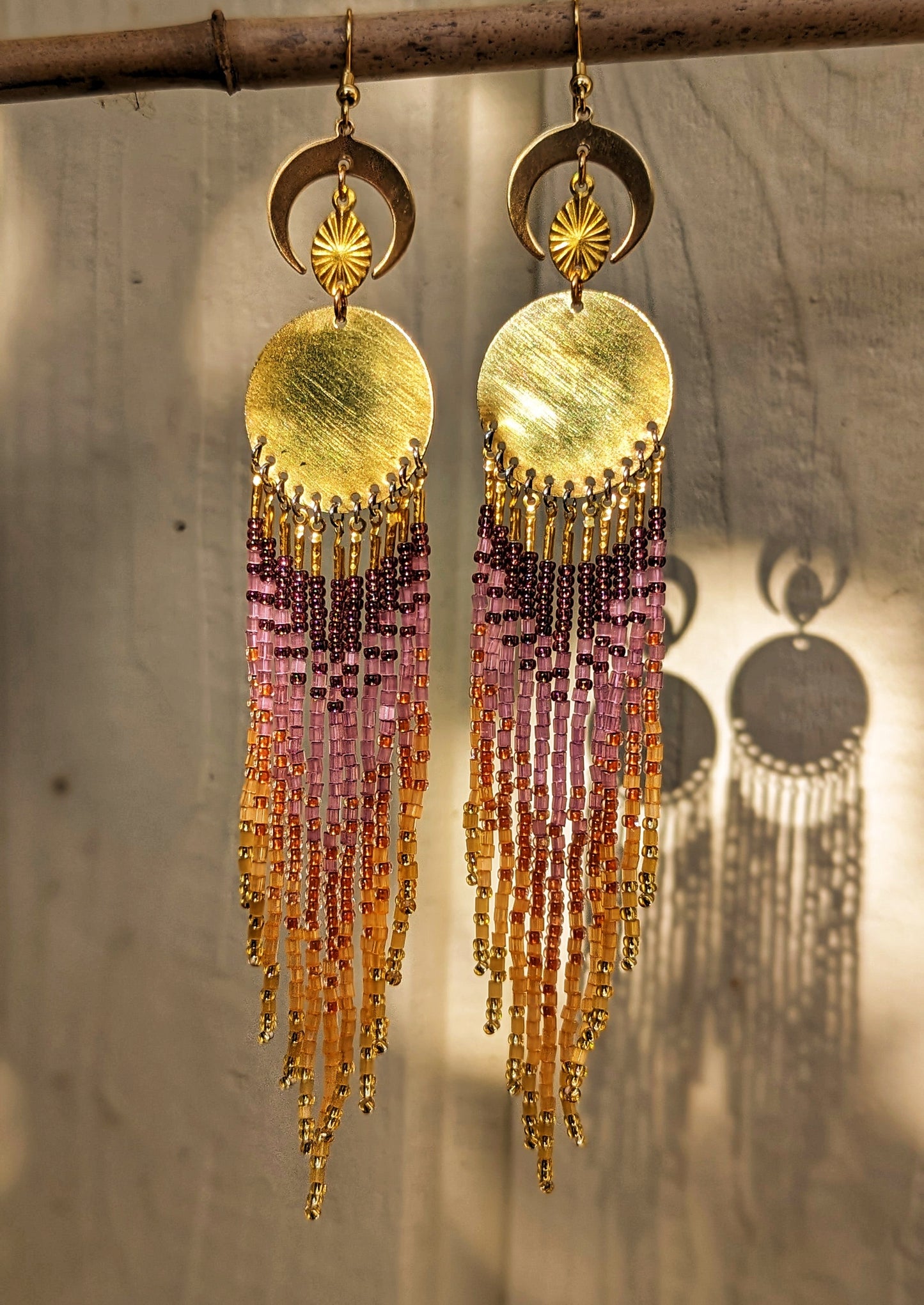 Moon & Milk earrings inspired by La Quebrada, featuring sunset-toned beadwork in gold, amber, and amethyst with brass moons and circular medallions.