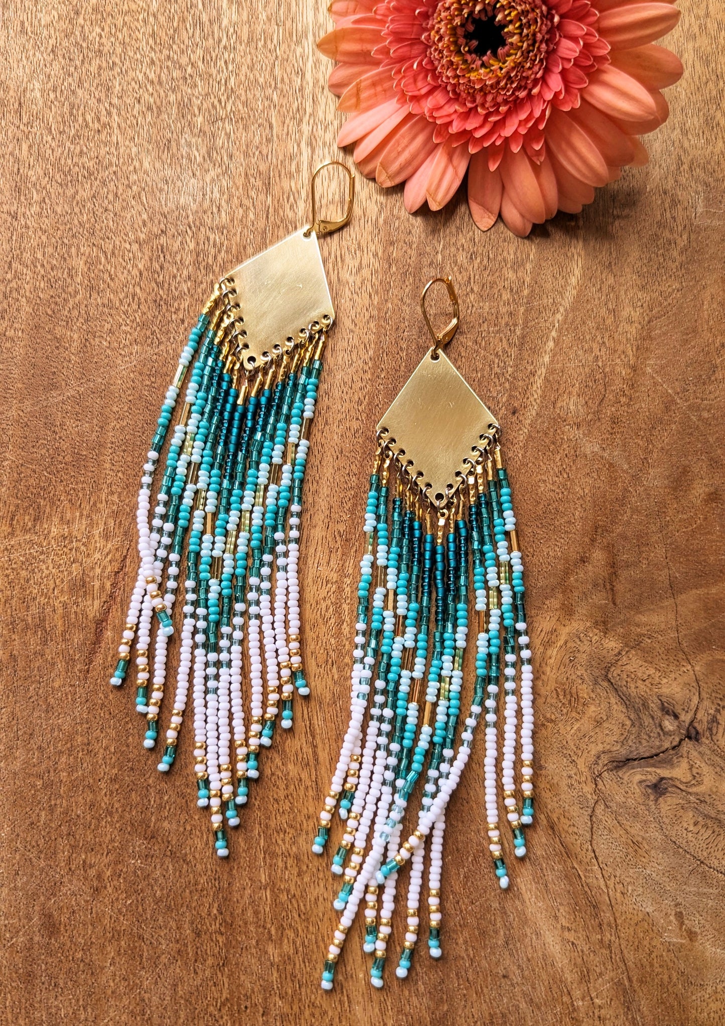 Moon & Milk turquoise, white, and gold seed bead earrings with brass findings, laid on wood with a coral flower—hand-beaded and coastal-inspired.