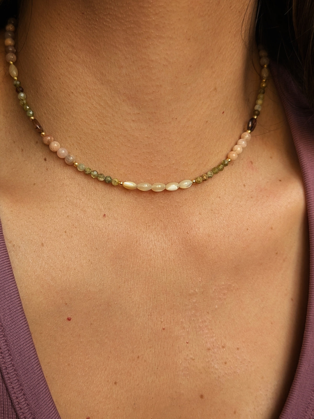 Gesmtone necklace with multicolored beads and mother-of-pearl on a person wearing a purple top.