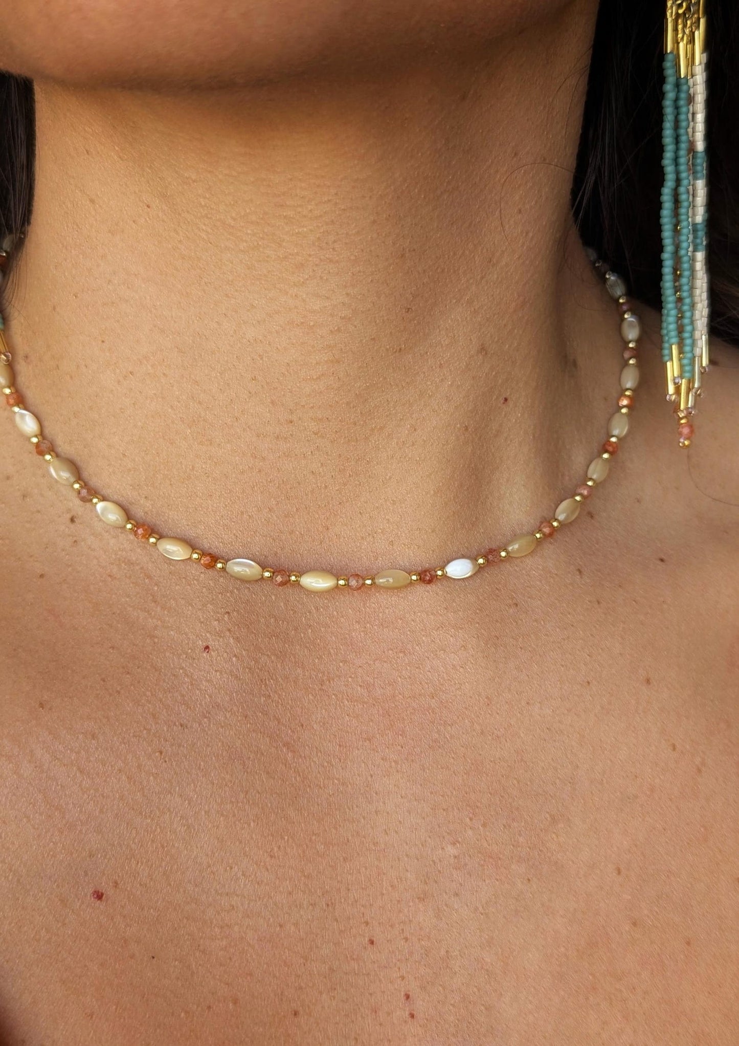 Close-up of a person wearing a mother-of-pearl beaded necklace with a blurred background.