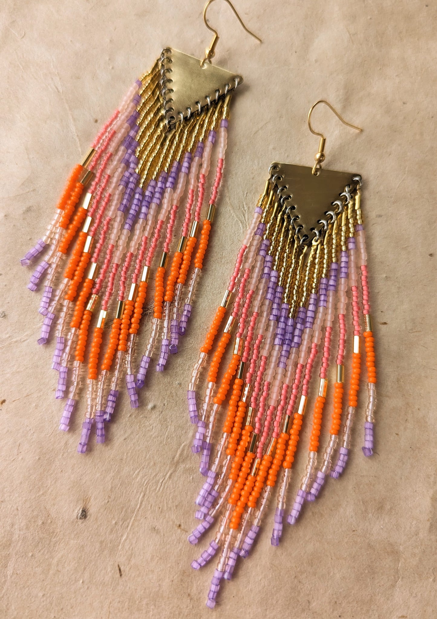 Orange Popsicle earrings by Moon & Milk with orange, lavender, pink, and peach seed beads, handcrafted into long fringe hanging from brass triangle tops.