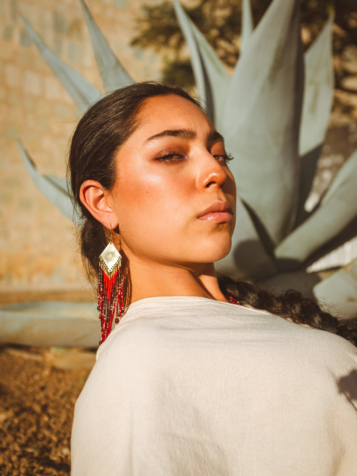 A woman with red beaded earrings lying in front of a cactus plant.