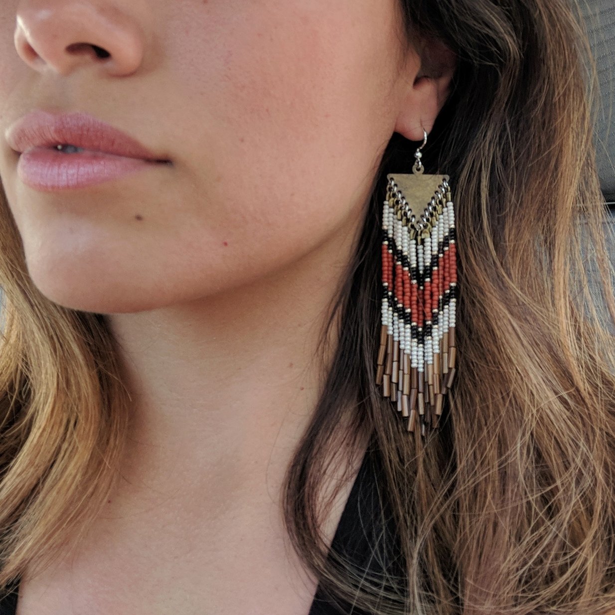 Model wearing terracotta bohemian earrings with brown fringes and a chevron design. -Moon & Milk