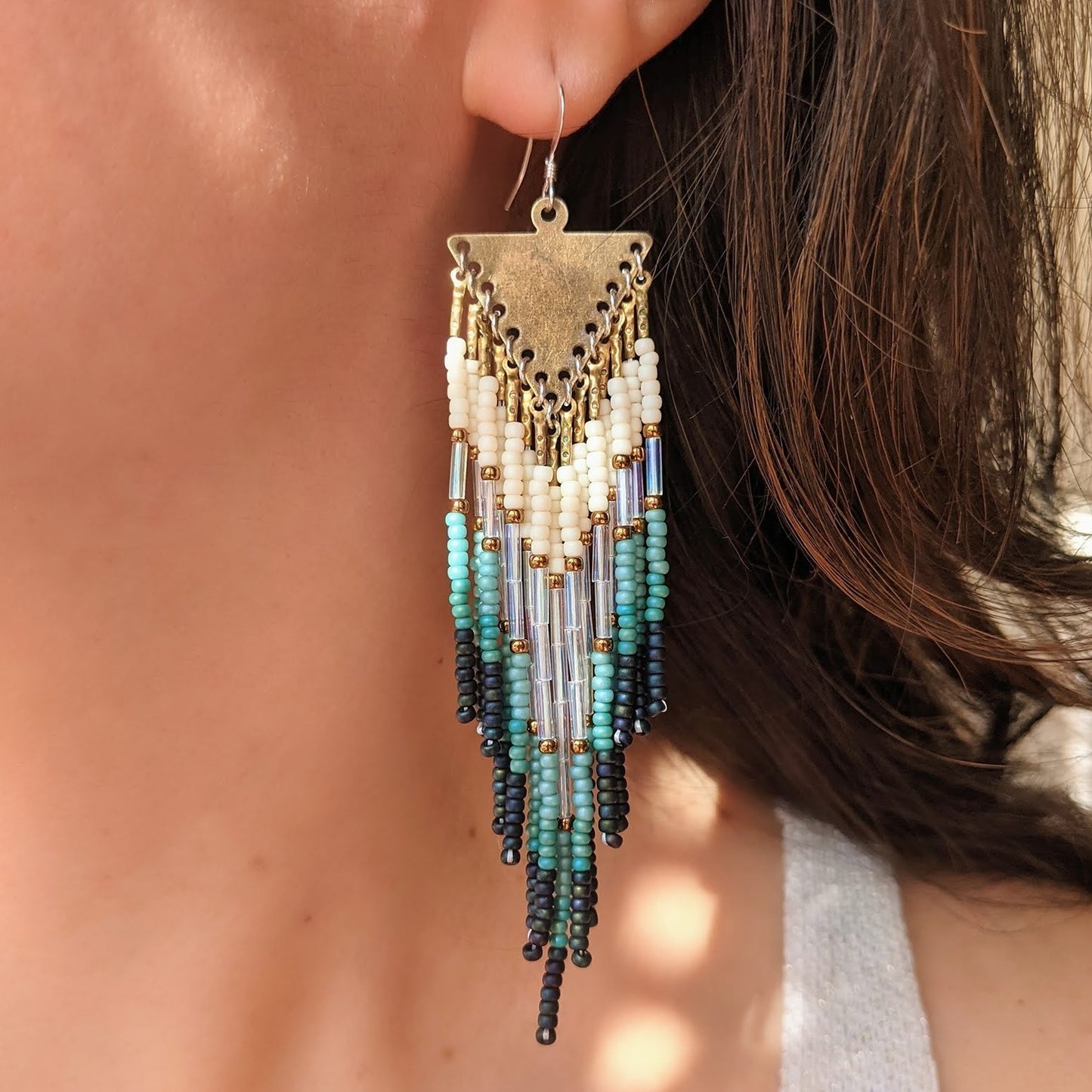 Moon & Milk artisan earrings featuring ivory, turquoise, and black seed beads with long glass bugles and brass details, worn by a model with dark hair.