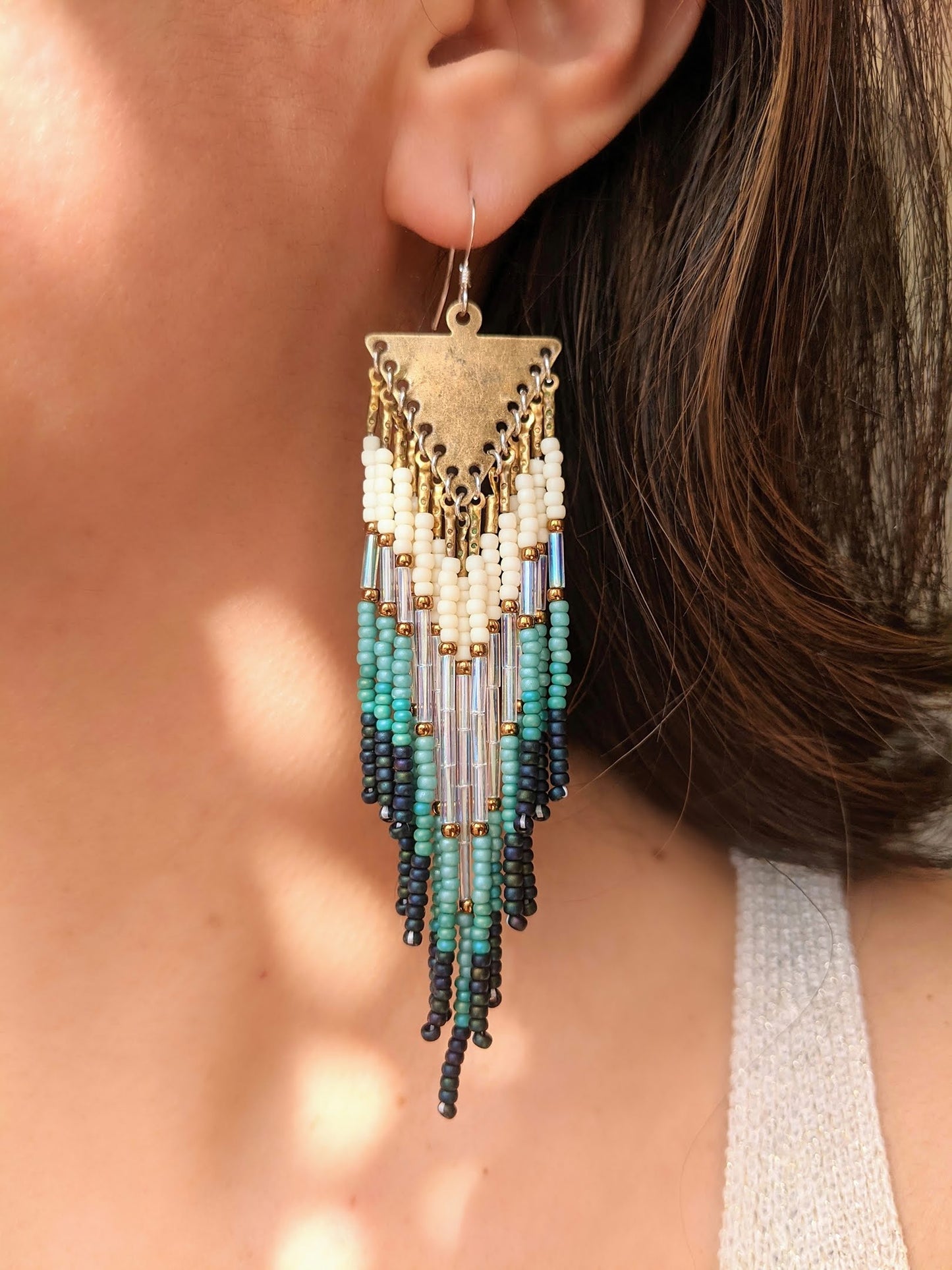 Moon & Milk artisan earrings featuring ivory, turquoise, and black seed beads with long glass bugles and brass details, worn by a model with dark hair.