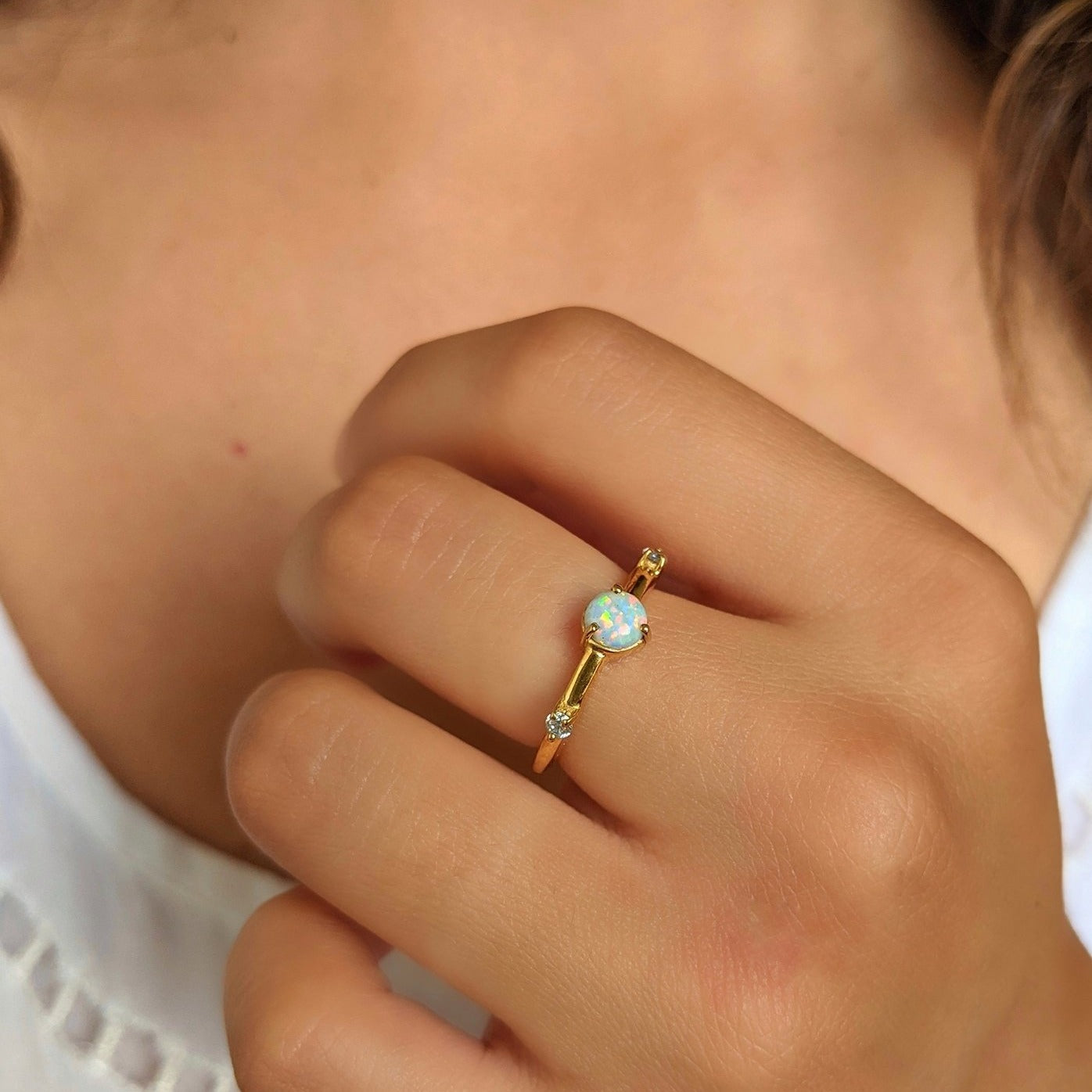 Gold-plated opal ring with a round iridescent center stone and CZ side accents, worn on a hand with natural lighting.