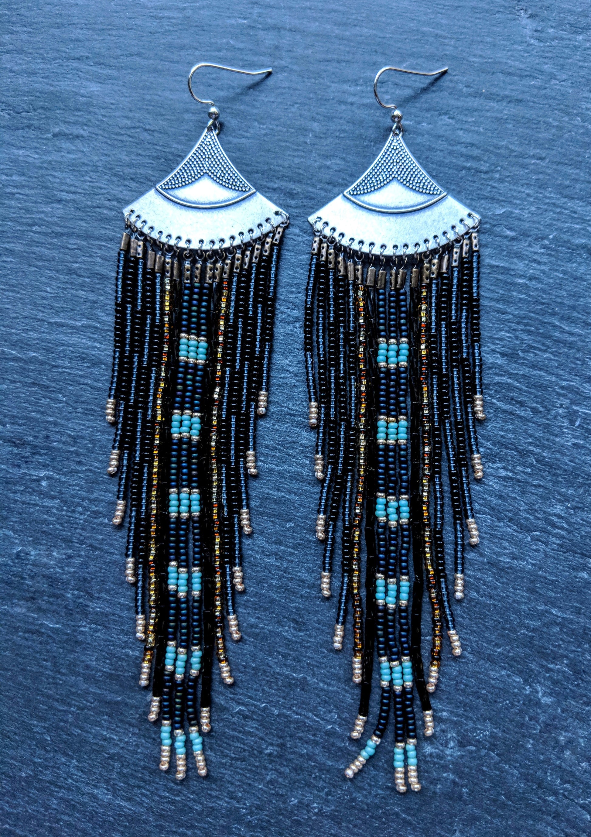 Moon & Milk long black and blue beaded earrings with silver fan tops and metallic accents, displayed on a slate-gray background.