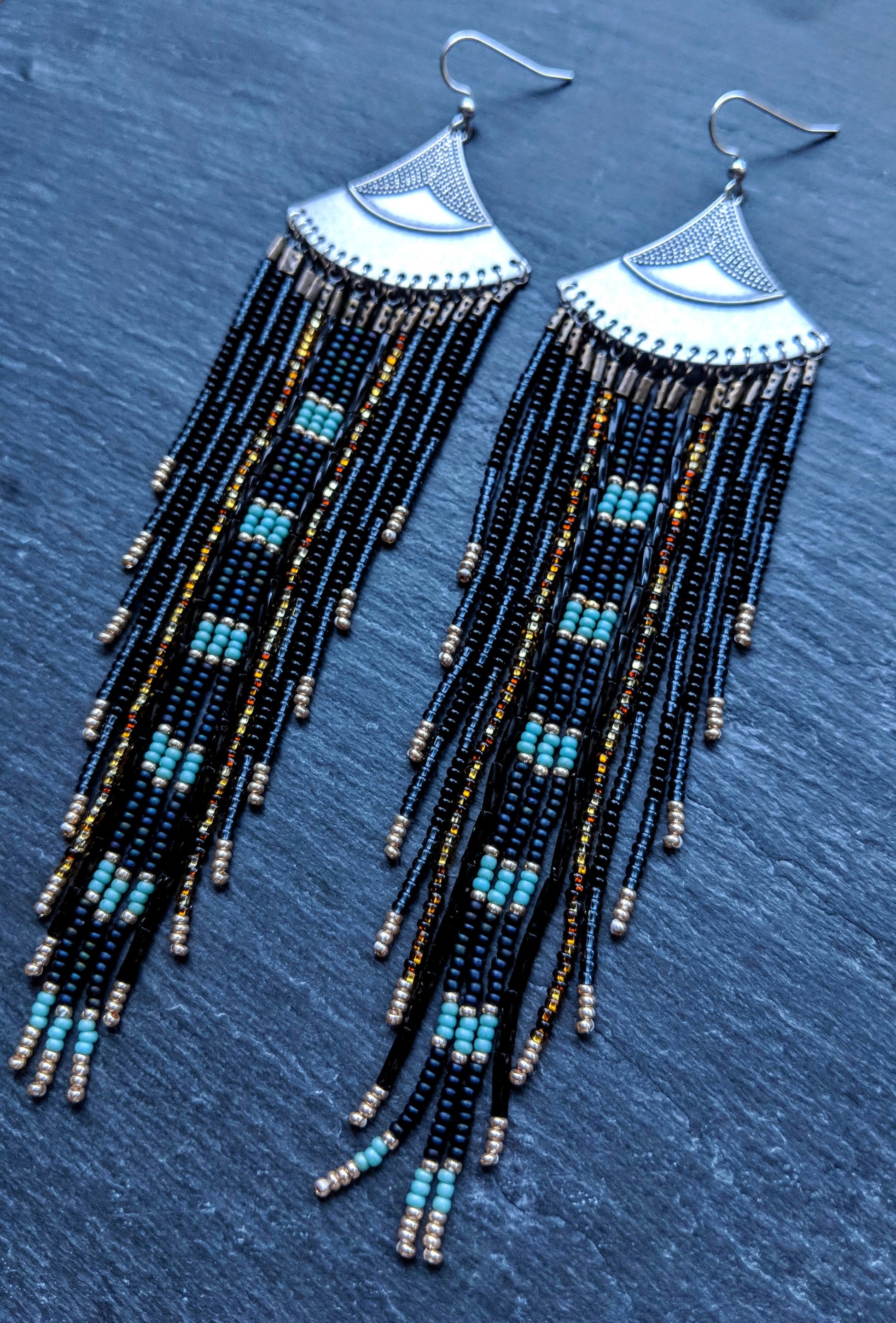 Moon & Milk long black and blue beaded earrings with silver fan tops and metallic accents, displayed on a slate-gray background.