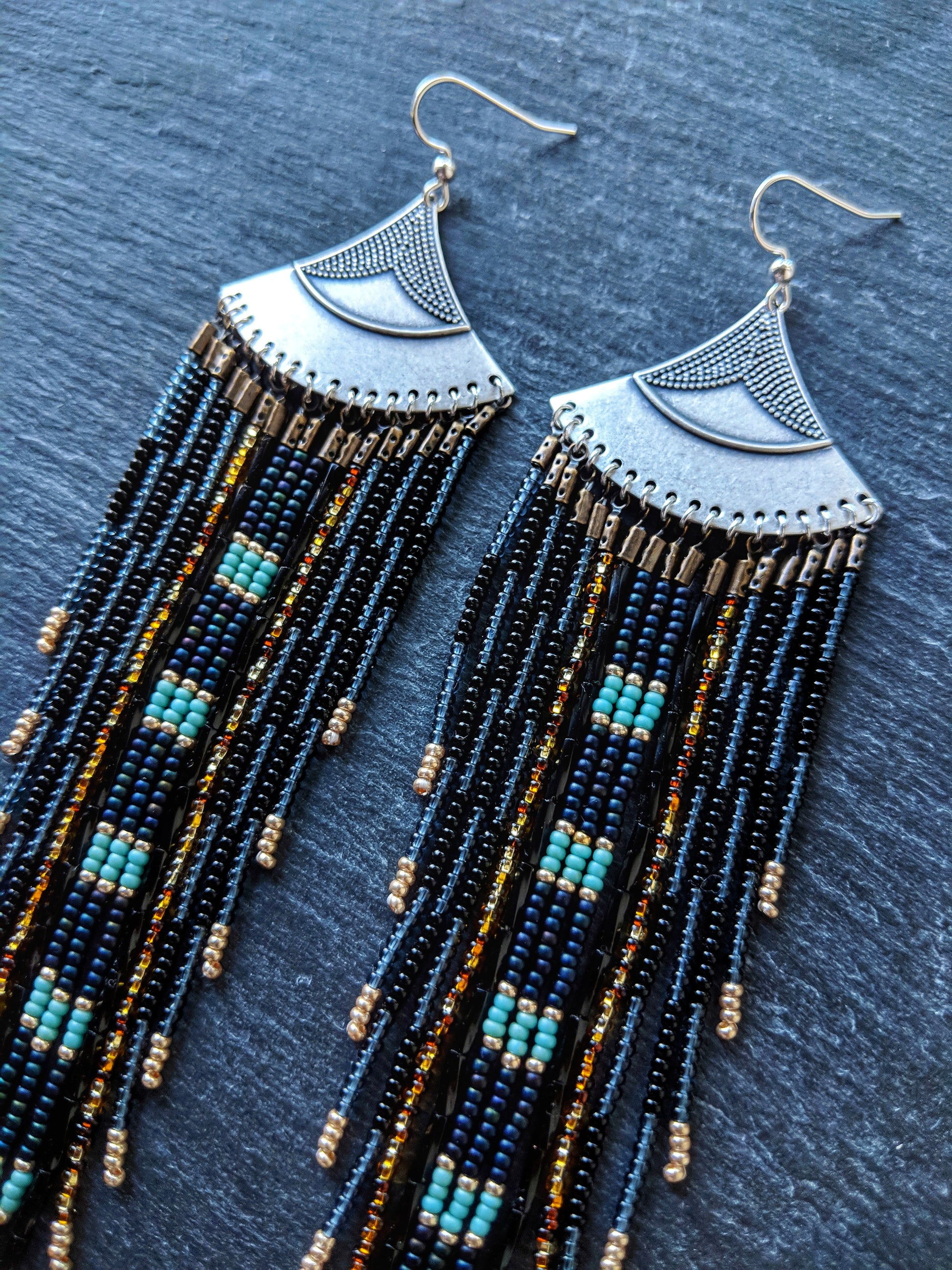 Moon & Milk long black and blue beaded earrings with silver fan tops and metallic accents, displayed on a slate-gray background.