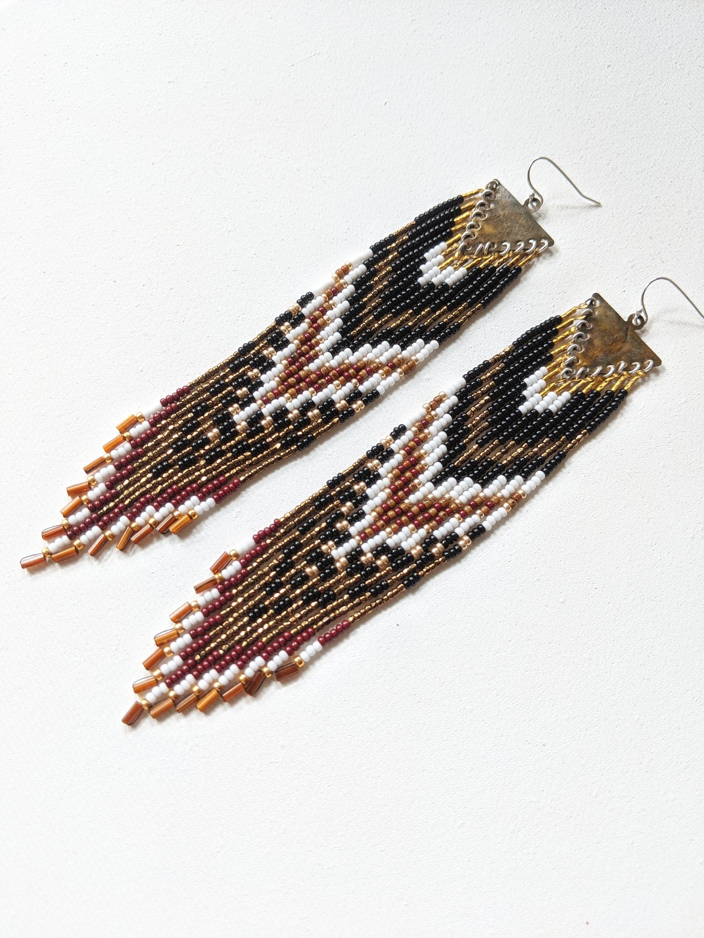 Artistic long native earrings from Moon & Milk with black, white, gold, and wine red beads. Handcrafted beadwork meets geometric brass jewelry design.