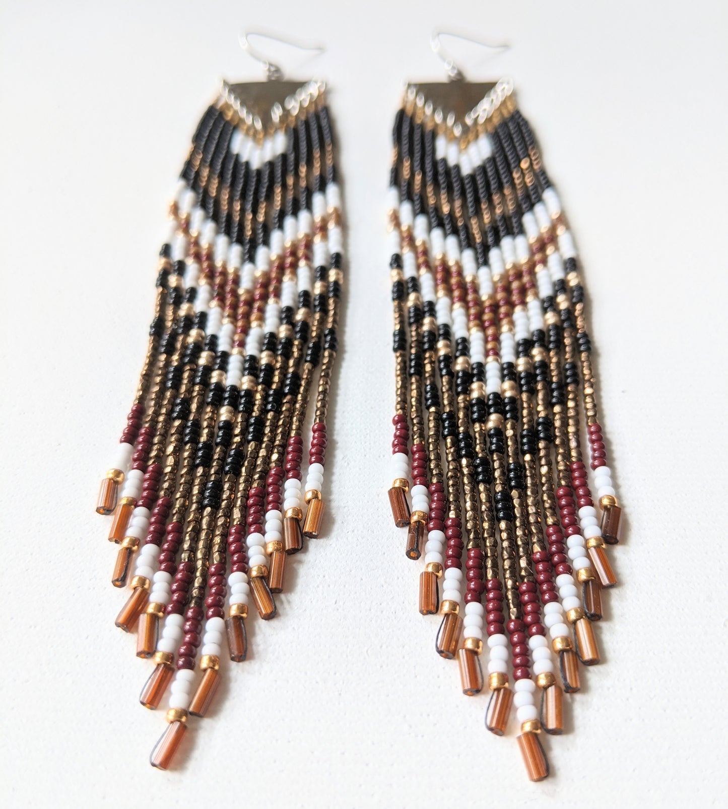 Artistic long native earrings from Moon & Milk with black, white, gold, and wine red beads. Handcrafted beadwork meets geometric brass jewelry design.
