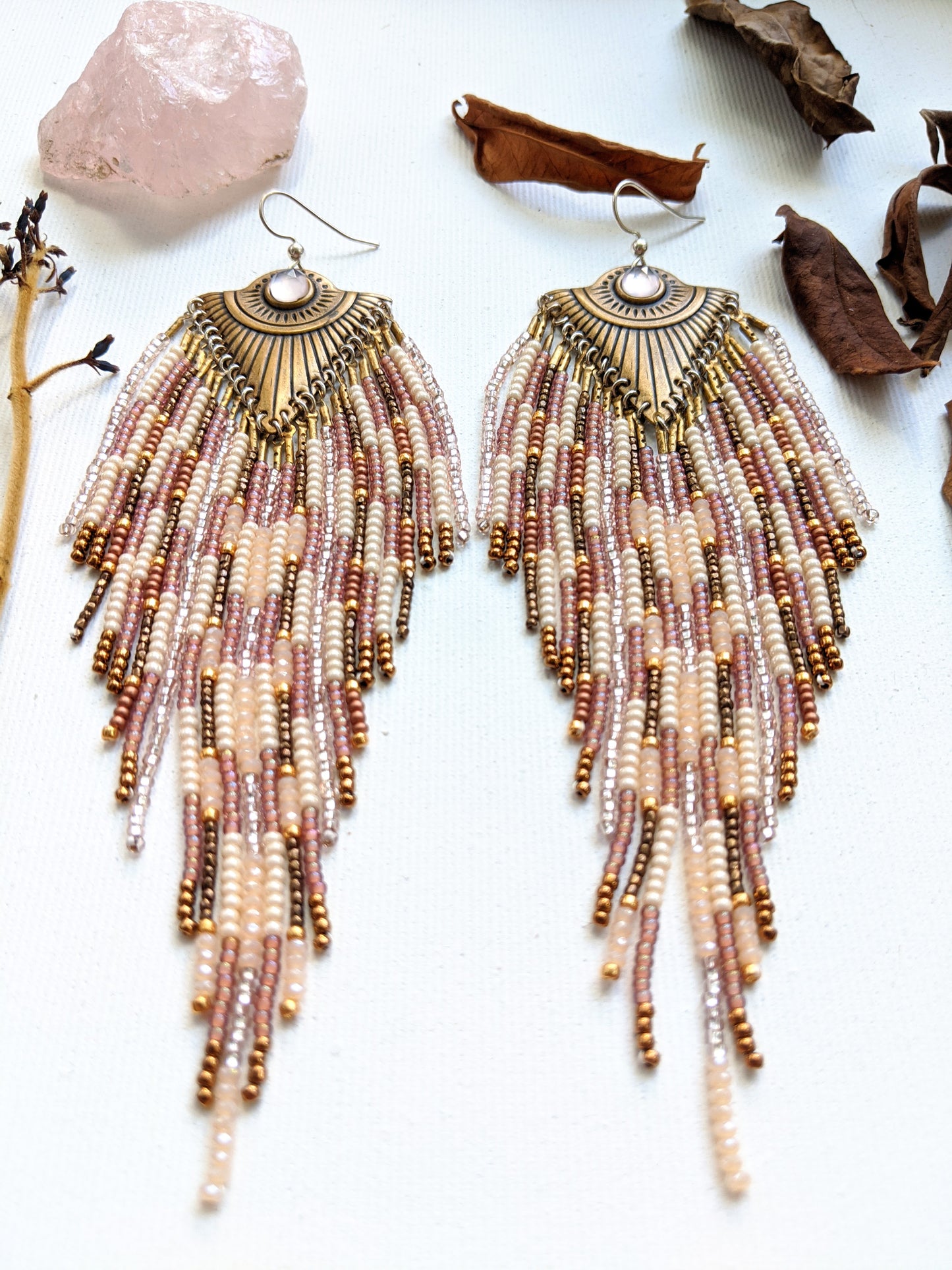 Moon & Milk long beaded earrings with brass fan-shaped medallions and cascading fringes of blush, cream, bronze, and rose gold beads on a white background.