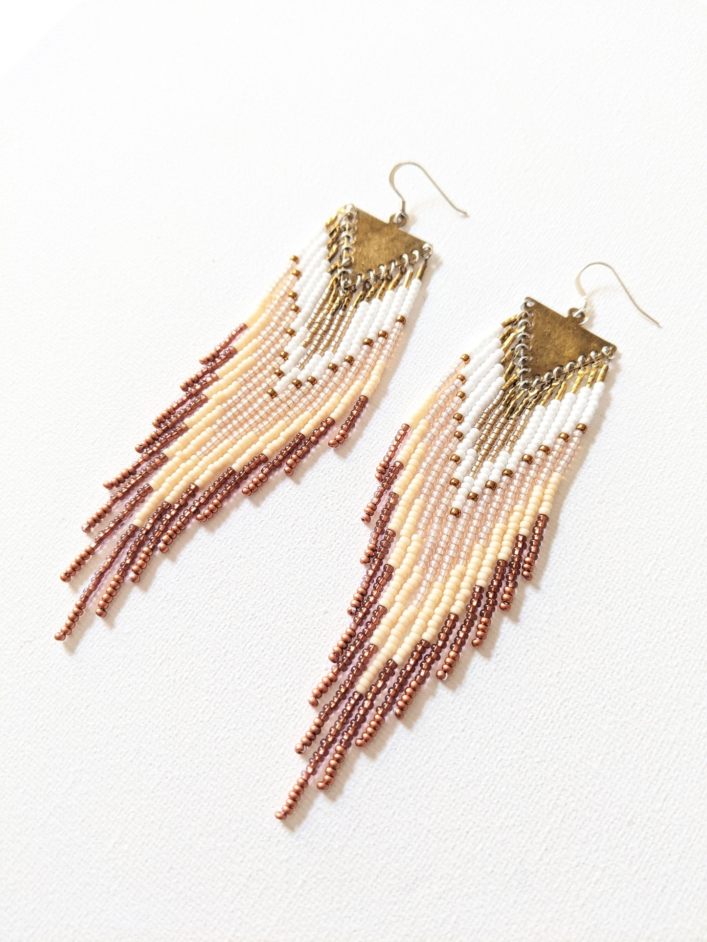 Handmade beaded fringe earrings by Moon & Milk with ivory, bronze, and white seed beads, suspended from brass triangle tops in a cascading pattern.