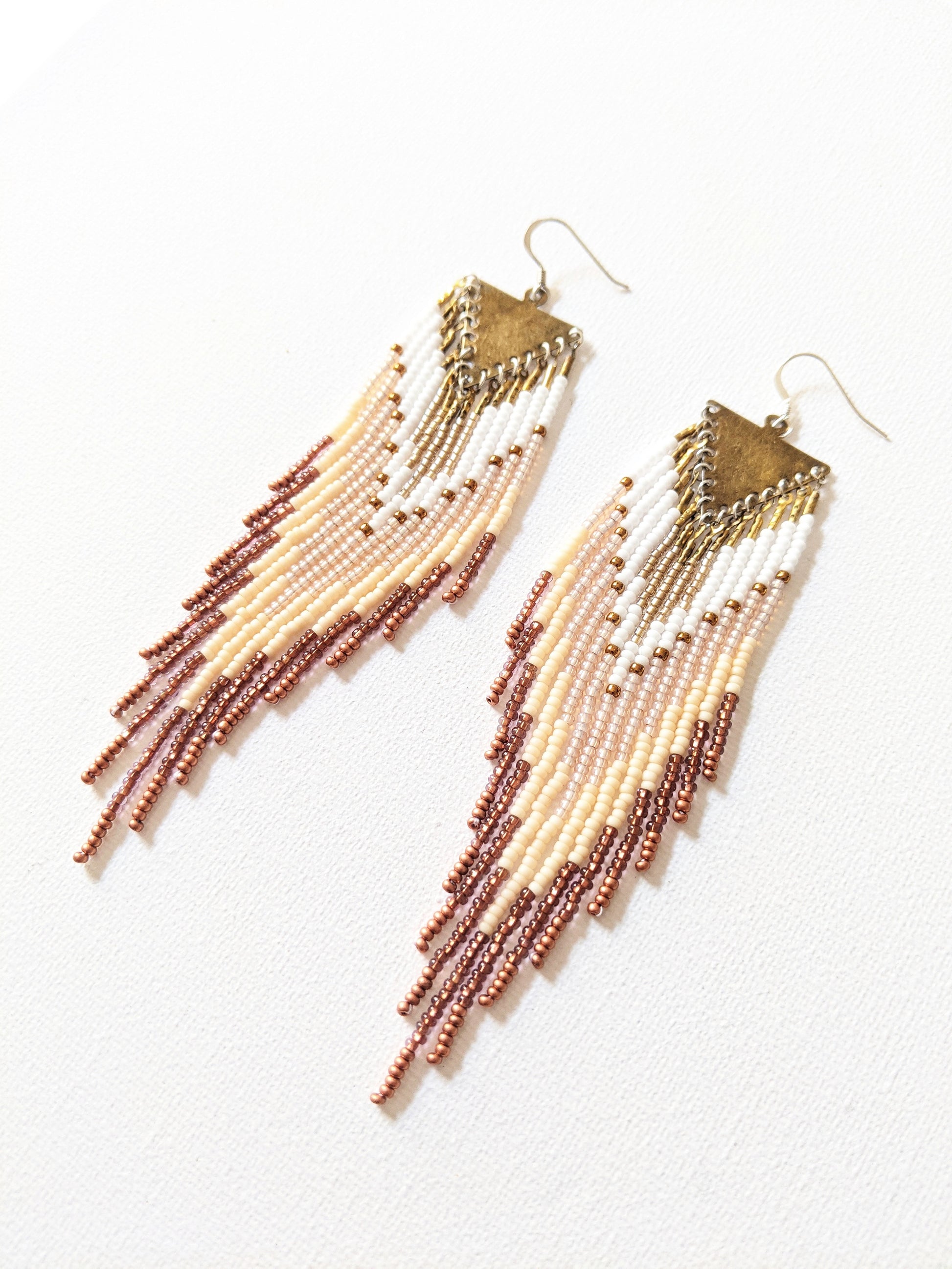 Handmade beaded fringe earrings by Moon & Milk with ivory, bronze, and white seed beads, suspended from brass triangle tops in a cascading pattern.