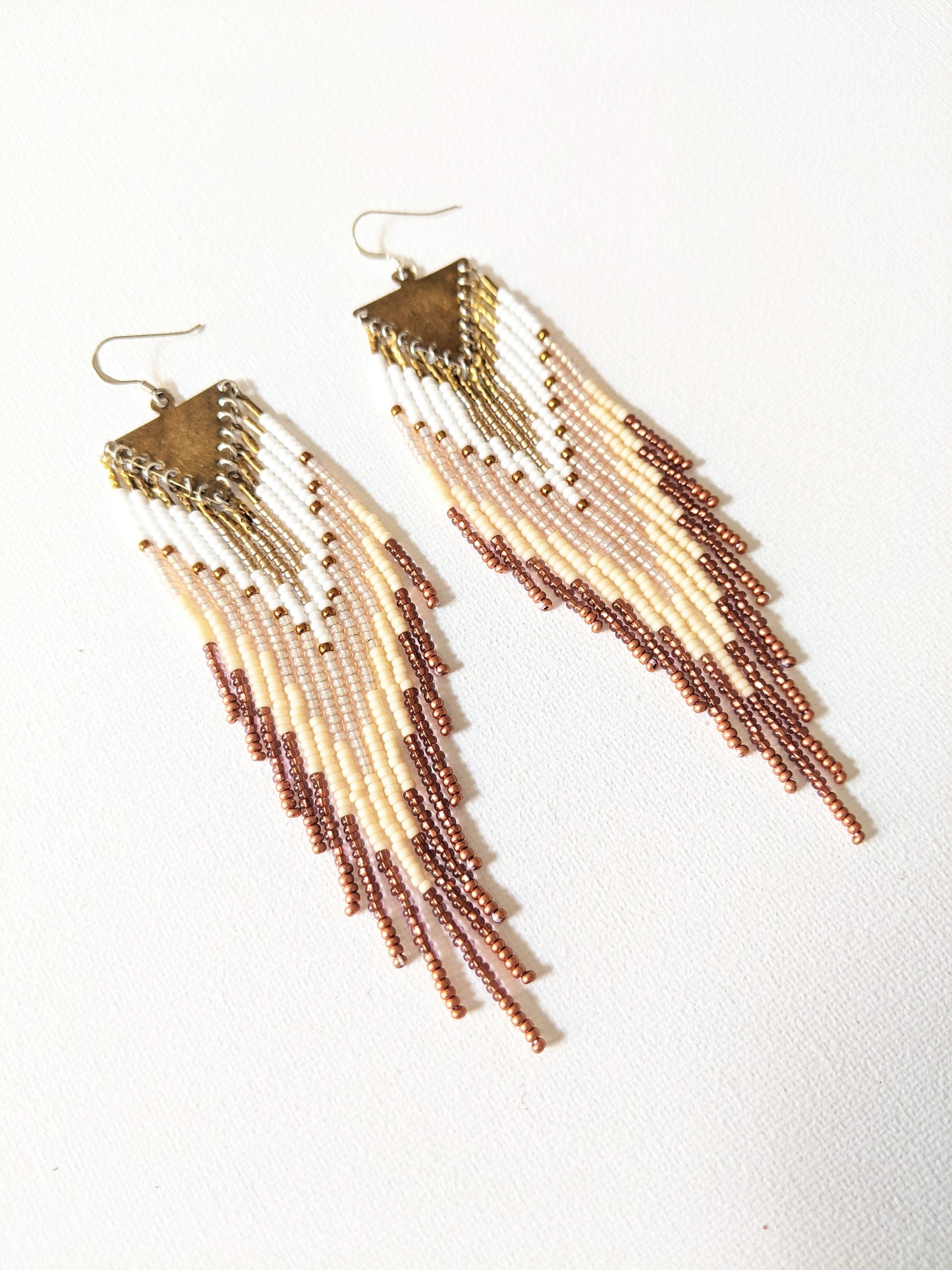 Handmade beaded fringe earrings by Moon & Milk with ivory, bronze, and white seed beads, suspended from brass triangle tops in a cascading pattern.
