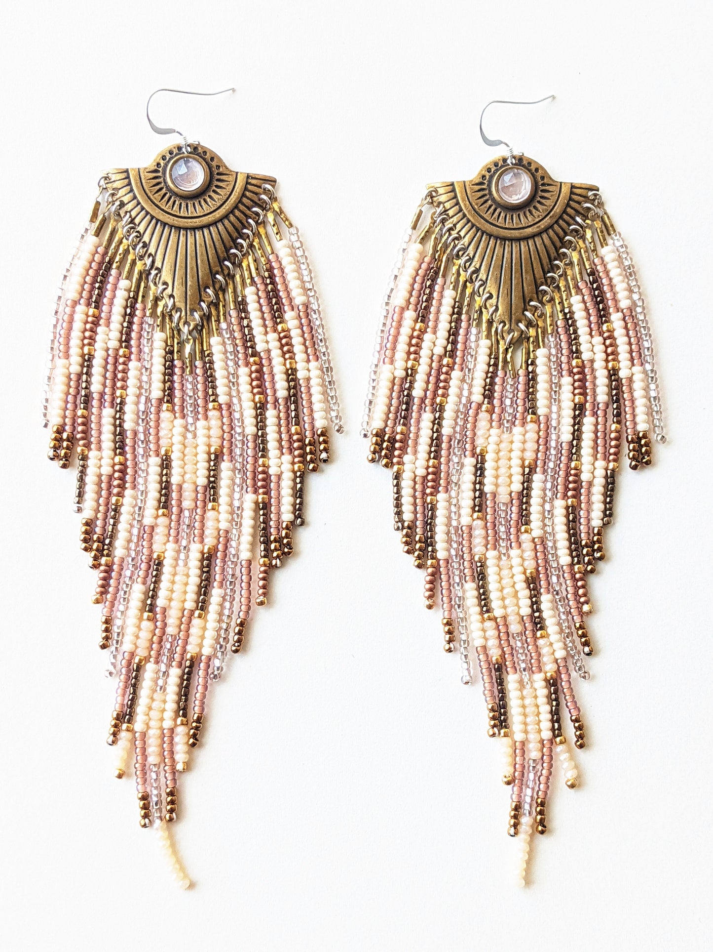 Moon & Milk long beaded earrings with brass fan-shaped medallions and cascading fringes of blush, cream, bronze, and rose gold beads on a white background.