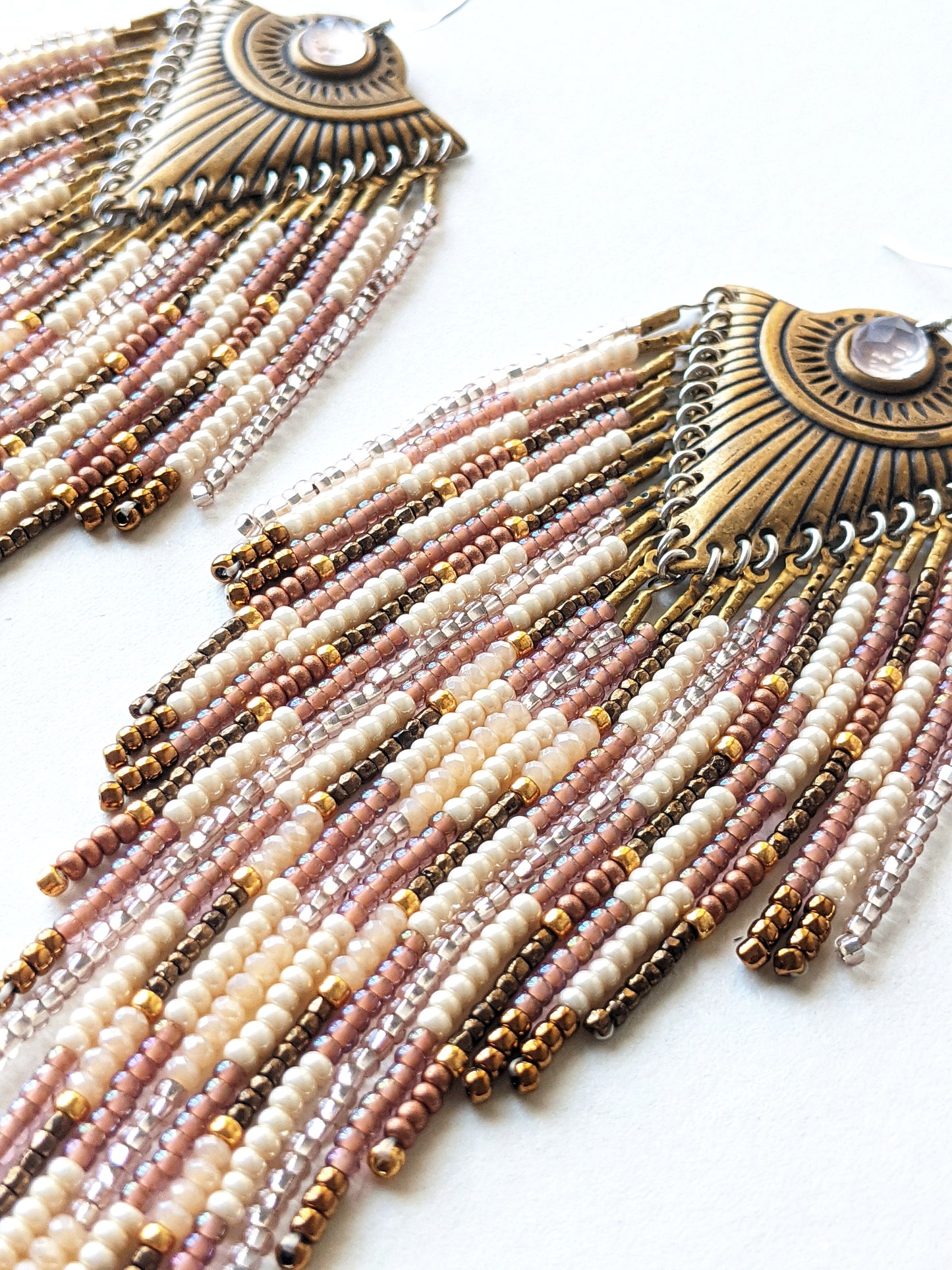 Moon & Milk long beaded earrings with brass fan-shaped medallions and cascading fringes of blush, cream, bronze, and rose gold beads on a white background.
