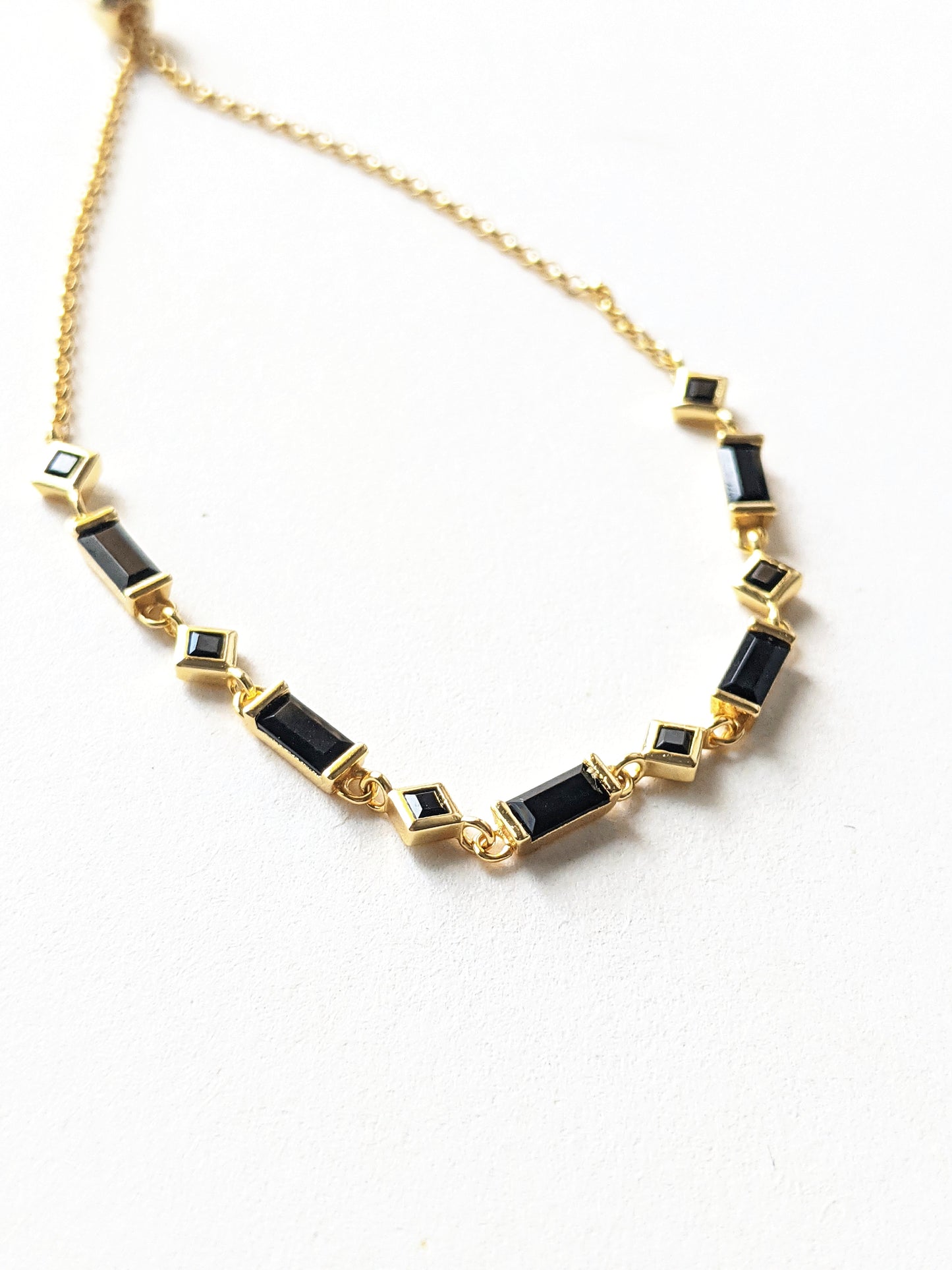 Gold chain bracelet with alternating black rectangular and square stones displayed flat on a white background with a gold slider clasp.