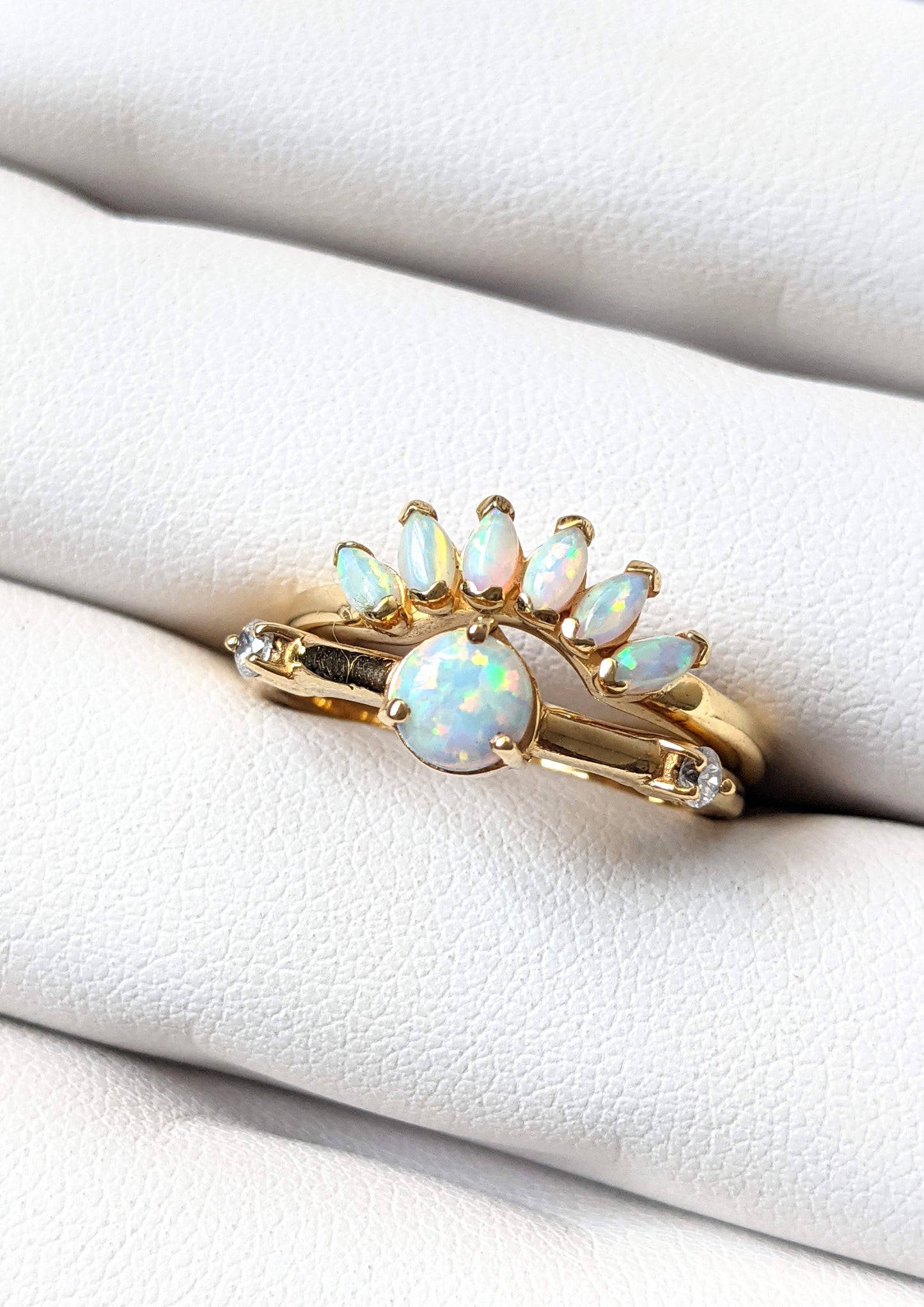 Gold-plated ring set featuring a round opal center stone and a curved crown of marquise opals, styled on a soft white ring display.