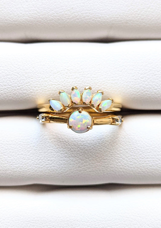 Gold-plated ring set featuring a round opal center stone and a curved crown of marquise opals, styled on a soft white ring display.