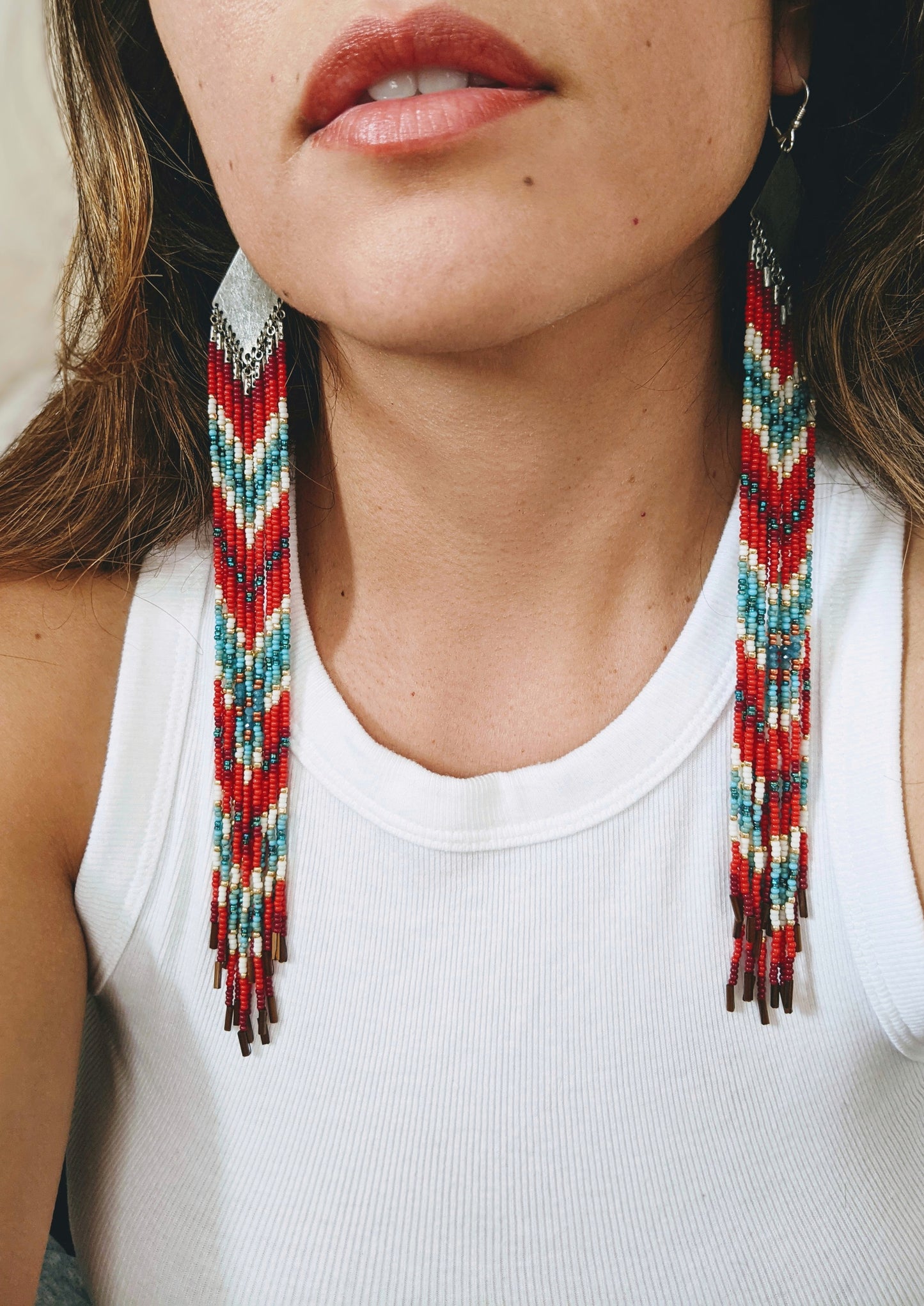 Moon & Milk - Model wearing long, beaded earrings with red, blue, gold, and white beads in a chevron pattern and silver tops. Styled with a white top.
