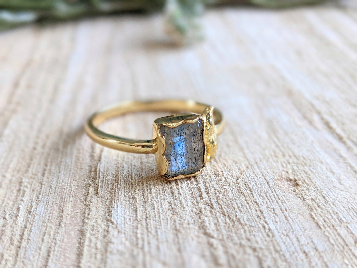 Close-up of a handcrafted labradorite ring with an organic gold bezel, resting on textured wood.