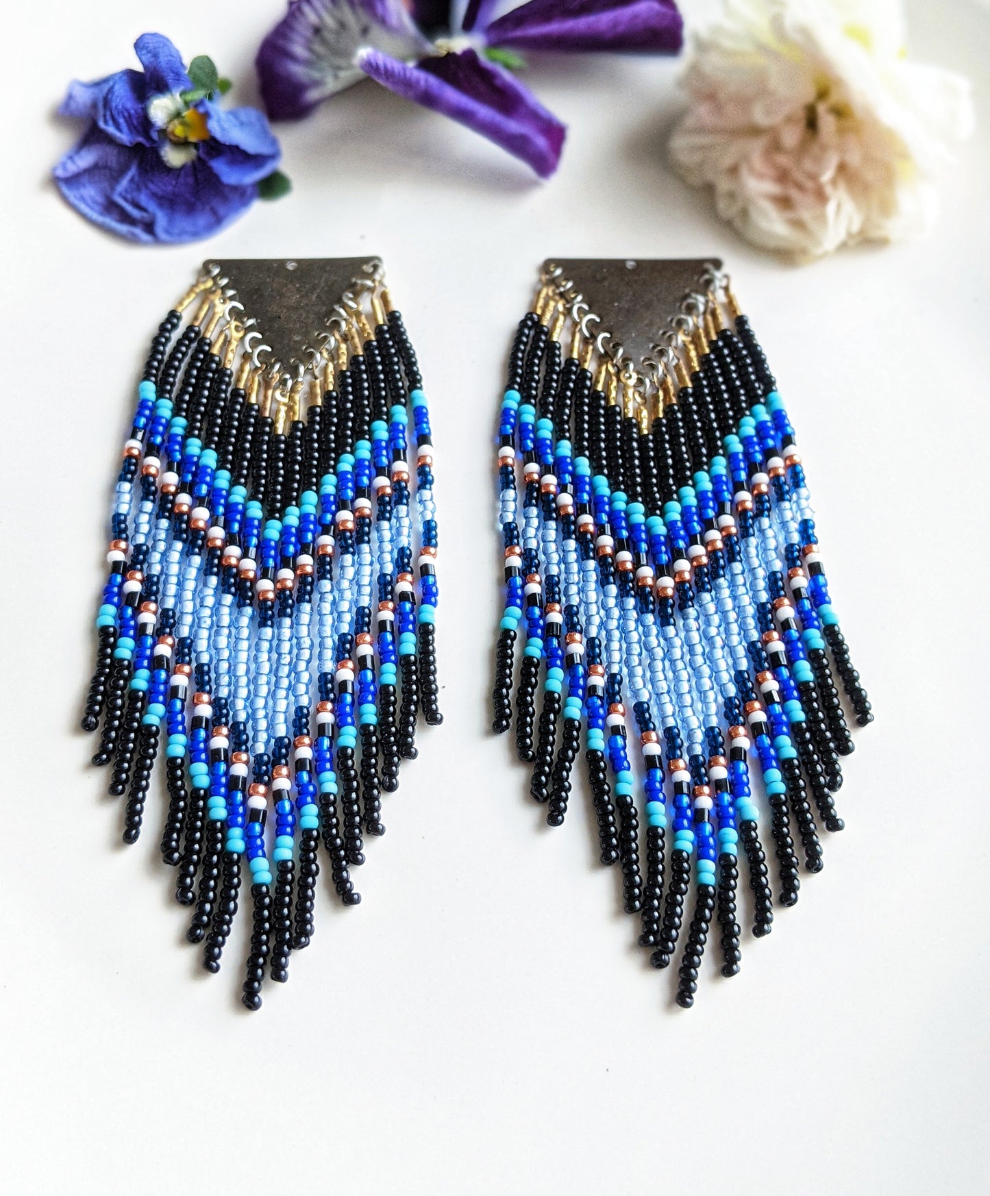 Moon & Milk handmade chevron beaded earrings in black, cobalt, and sky blue with metallic accents, styled on a white plate with fresh flowers.