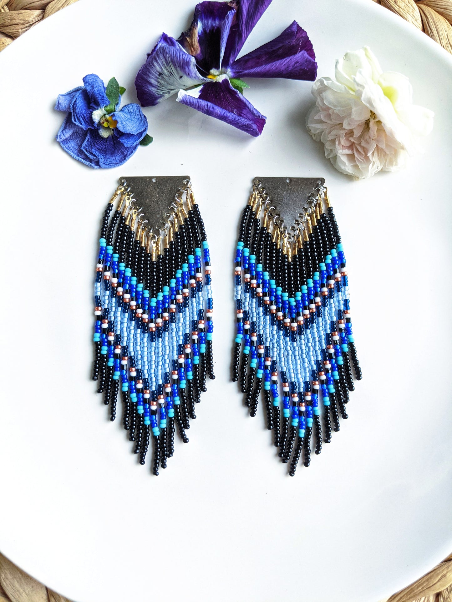Moon & Milk handmade chevron beaded earrings in black, cobalt, and sky blue with metallic accents, styled on a white plate with fresh flowers.