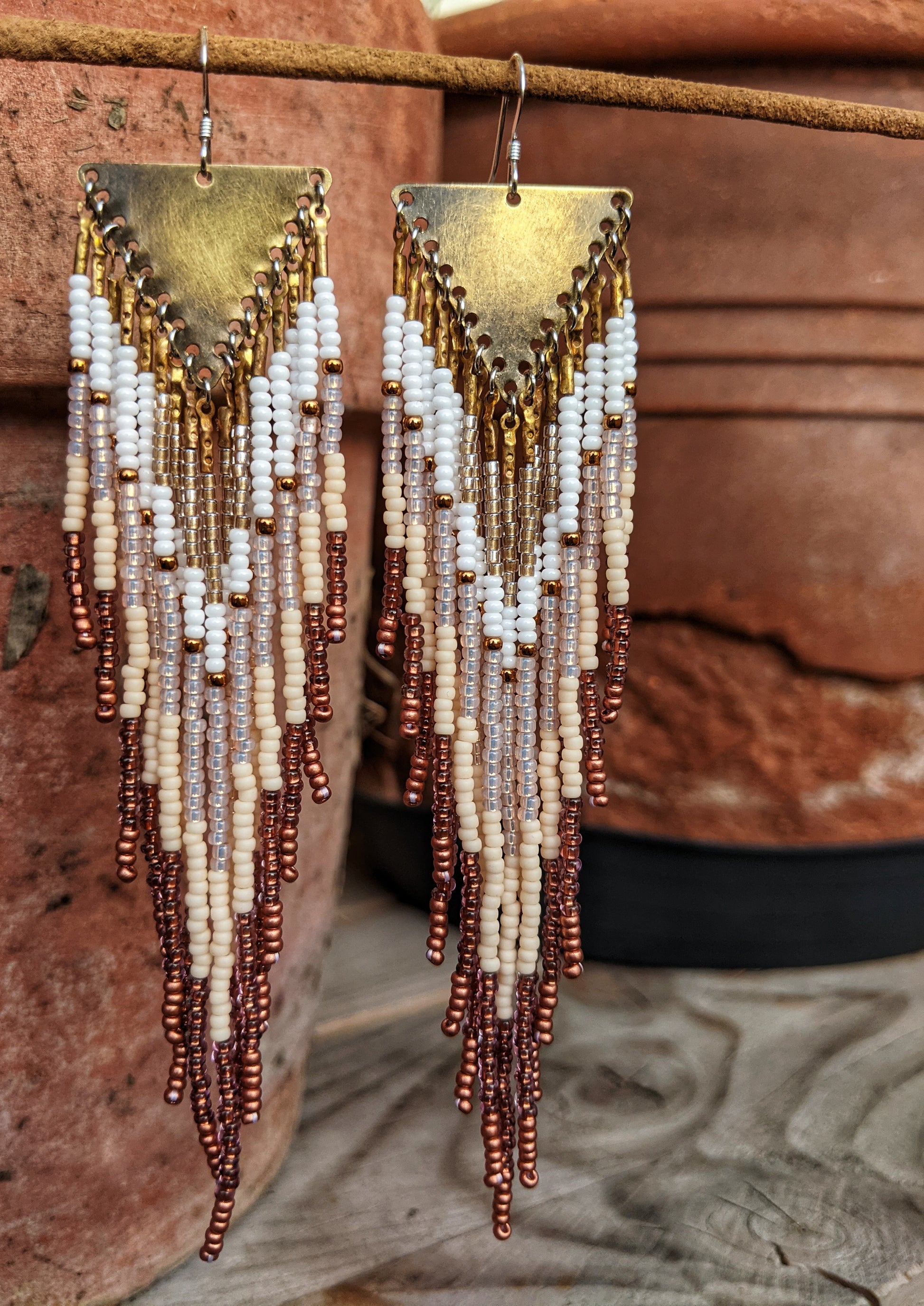 Handmade beaded fringe earrings by Moon & Milk with ivory, bronze, and white seed beads, suspended from brass triangle tops in a cascading pattern.