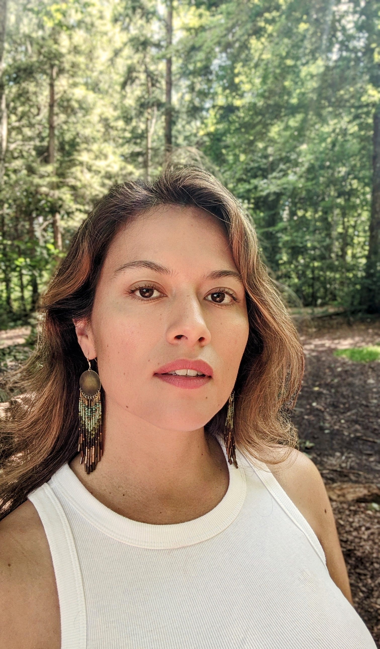 Moon & Milk handcrafted earrings with round brass tops, green and brown beadwork, and layered bamboo bugle fringe worn by a woman.