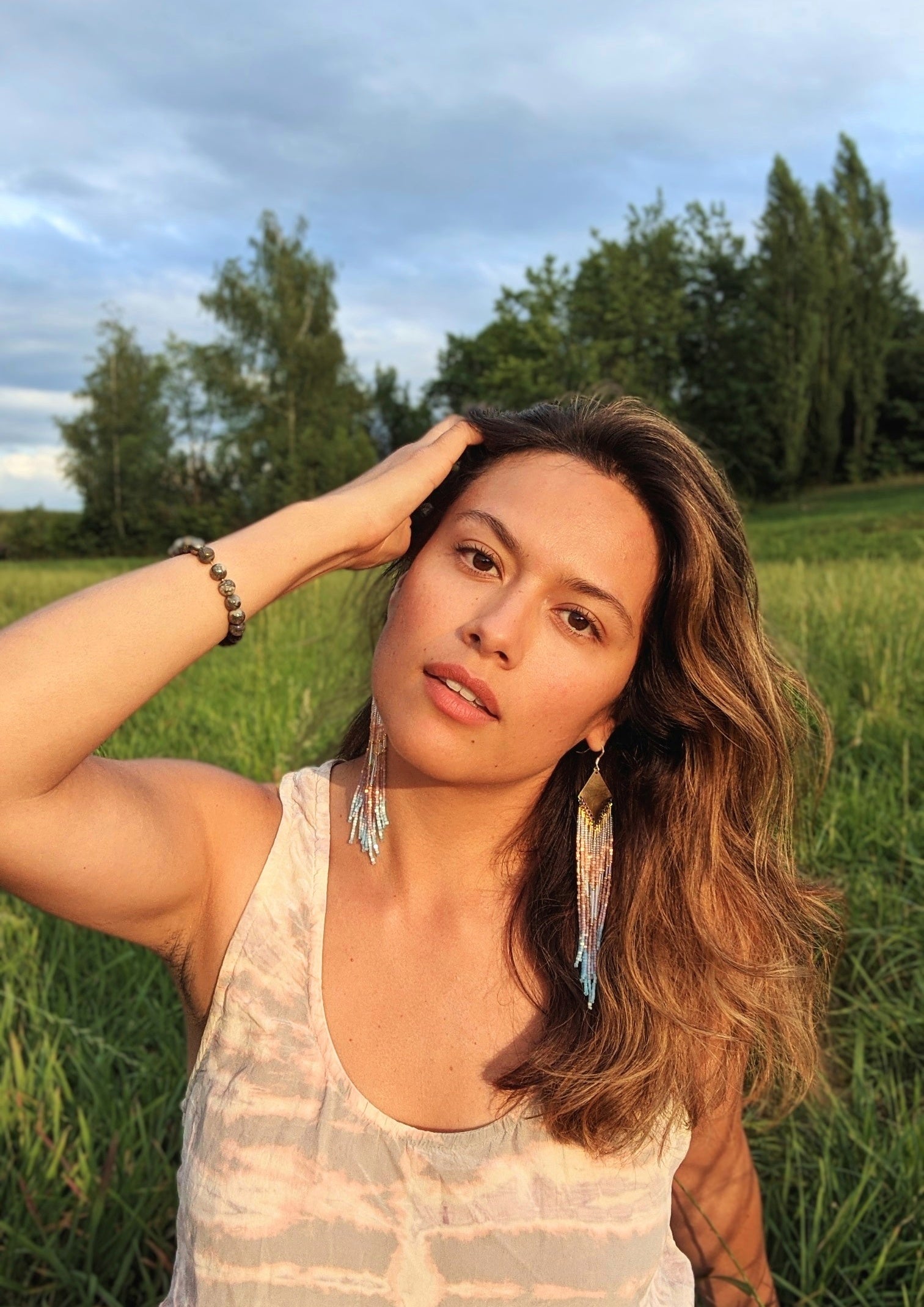Woman wearing Moon & Milk's artisan earrings handcrafted with satin hex-cut beads, brass, and sterling silver. Soft pastel beadwork in a long native earring design.