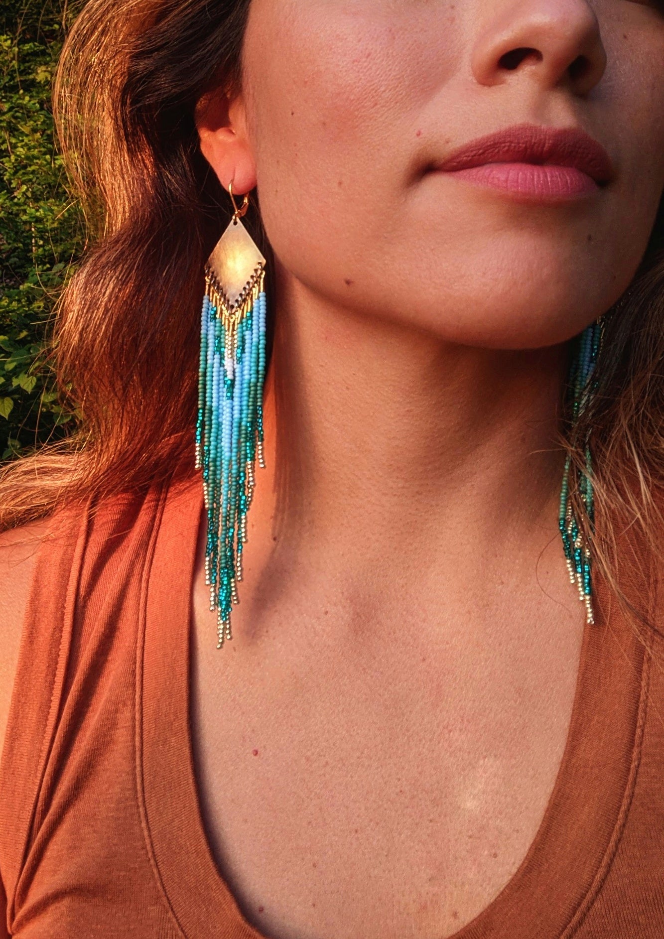Handcrafted beaded earrings by Moon & Milk featuring cascading turquoise, sea green, and gold strands, inspired by the landscapes of Switzerland., worn by a woman.