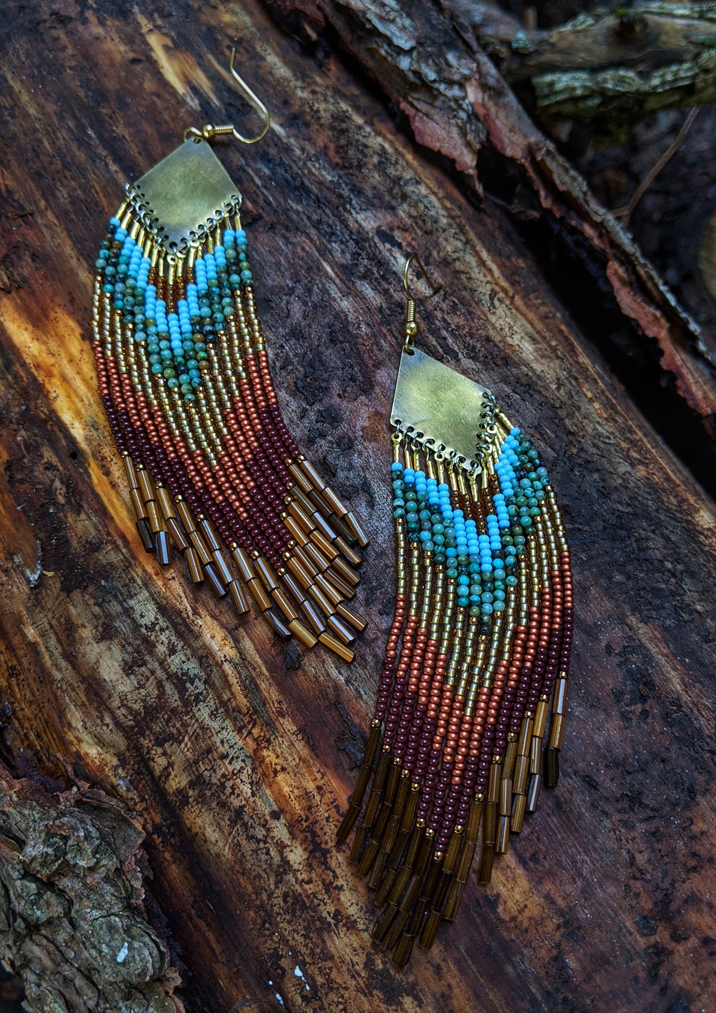 Moon & Milk - Long boho beaded earrings with turquoise, brown, gold, and maroon beads in a chevron pattern. Gold diamond-shaped tops. Photographed on a tree trunk.