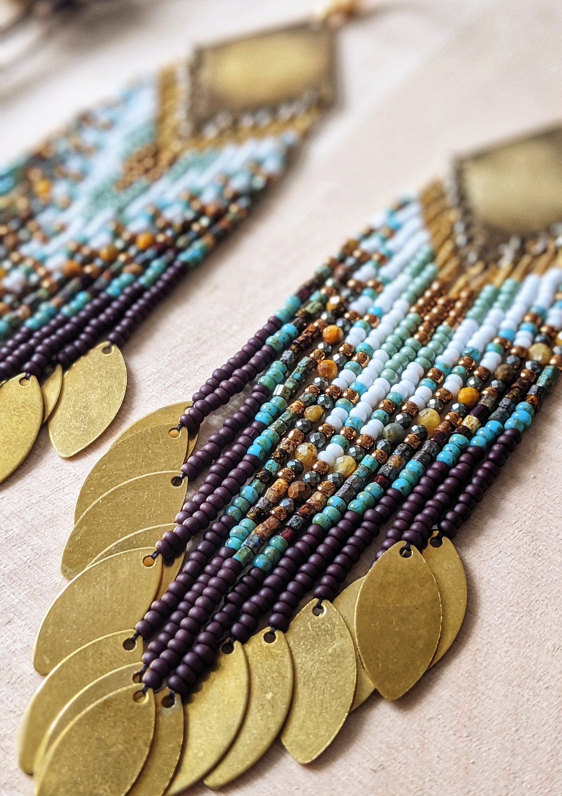 Handcrafted beaded earrings by Moon & Milk with brass diamond tops, seed bead fringe in brown, turquoise, and white, and golden brass disc charms.