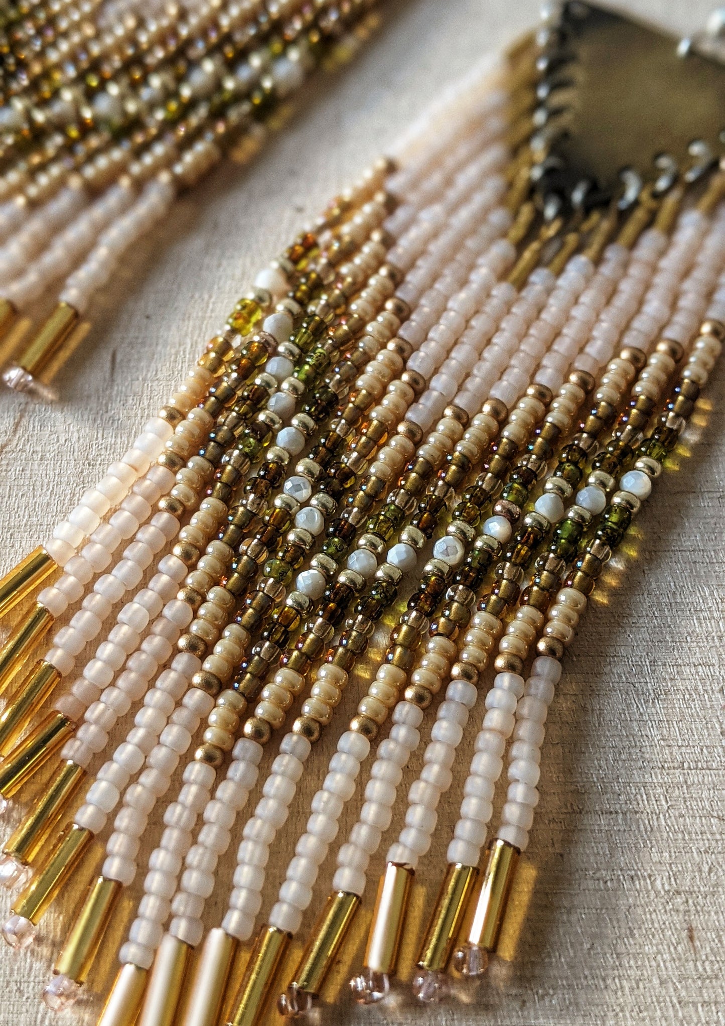 Moon & Milk handmade beaded earrings with cream, gold, olive, Mother of Pearl, and white beadwork in a chevron pattern, finished with brass findings and soft pink tips.