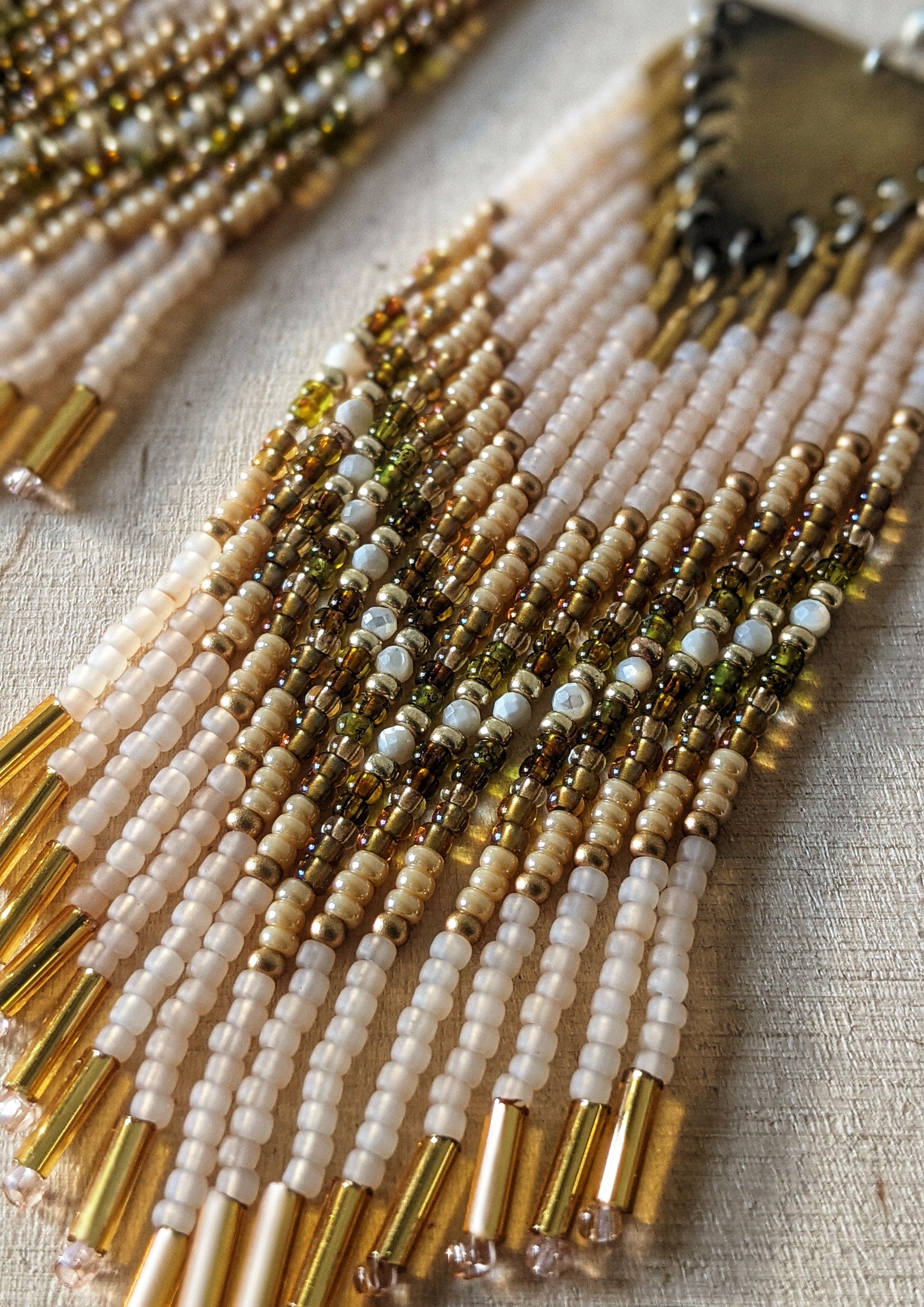 Moon & Milk handmade beaded earrings with cream, gold, olive, Mother of Pearl, and white beadwork in a chevron pattern, finished with brass findings and soft pink tips.