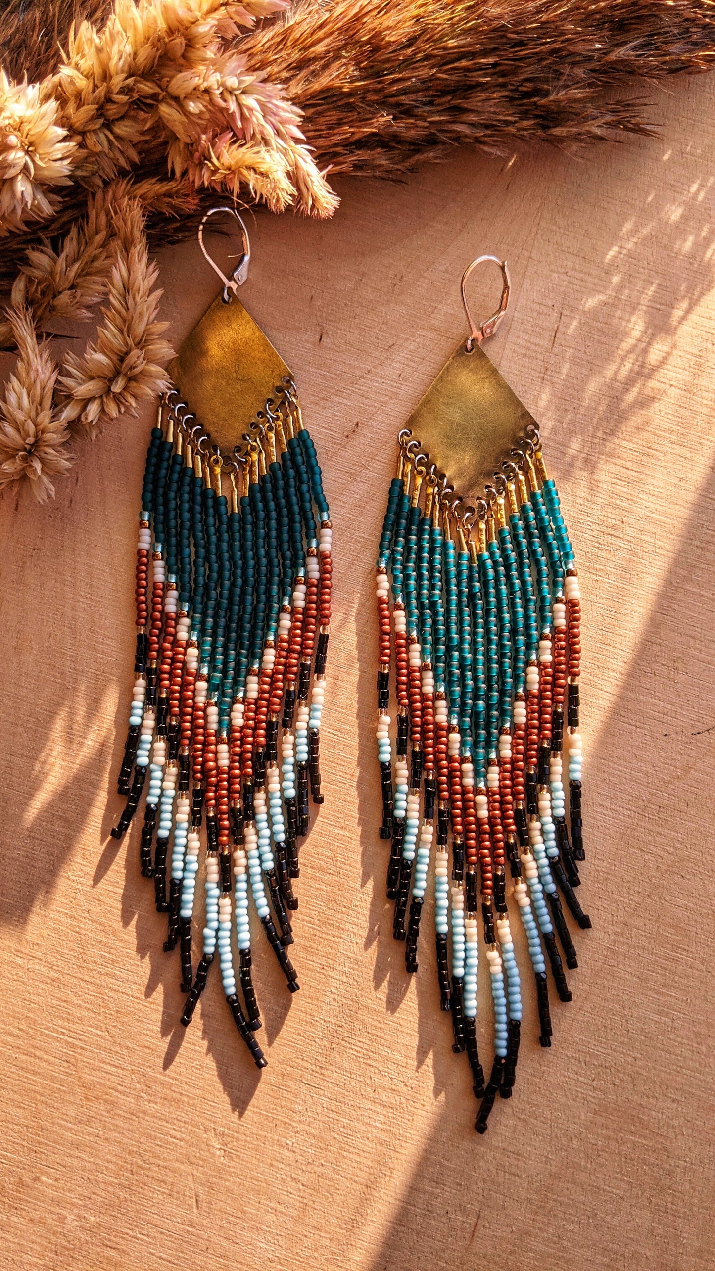 Beaded statement earrings with a bold chevron pattern in teal, rust, black, and ivory. Features intricate beadwork with a brass diamond-shaped top.