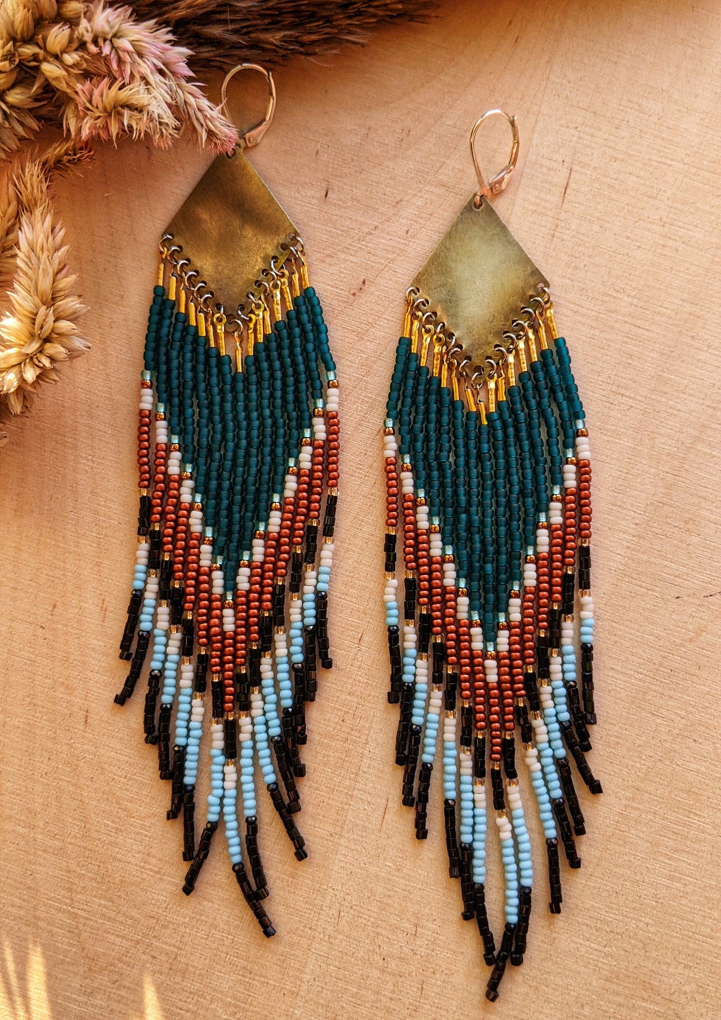 Beaded statement earrings with a bold chevron pattern in teal, rust, black, and ivory. Features intricate beadwork with a brass diamond-shaped top.