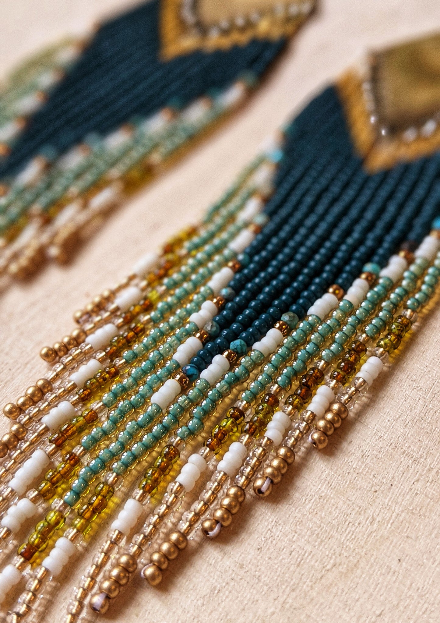 Close-up of Moon & Milk handcrafted beaded earrings with dark green, gold, turquoise stones, cream glass beads, and brass accents.