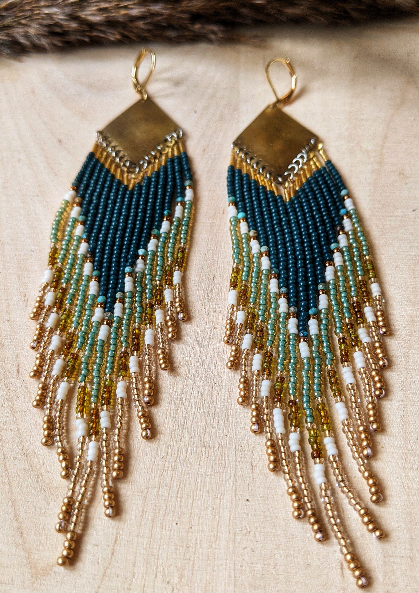 Close-up of  Moon & Milk handcrafted beaded earrings with dark green, gold, turquoise stones, cream glass beads, and brass accents.