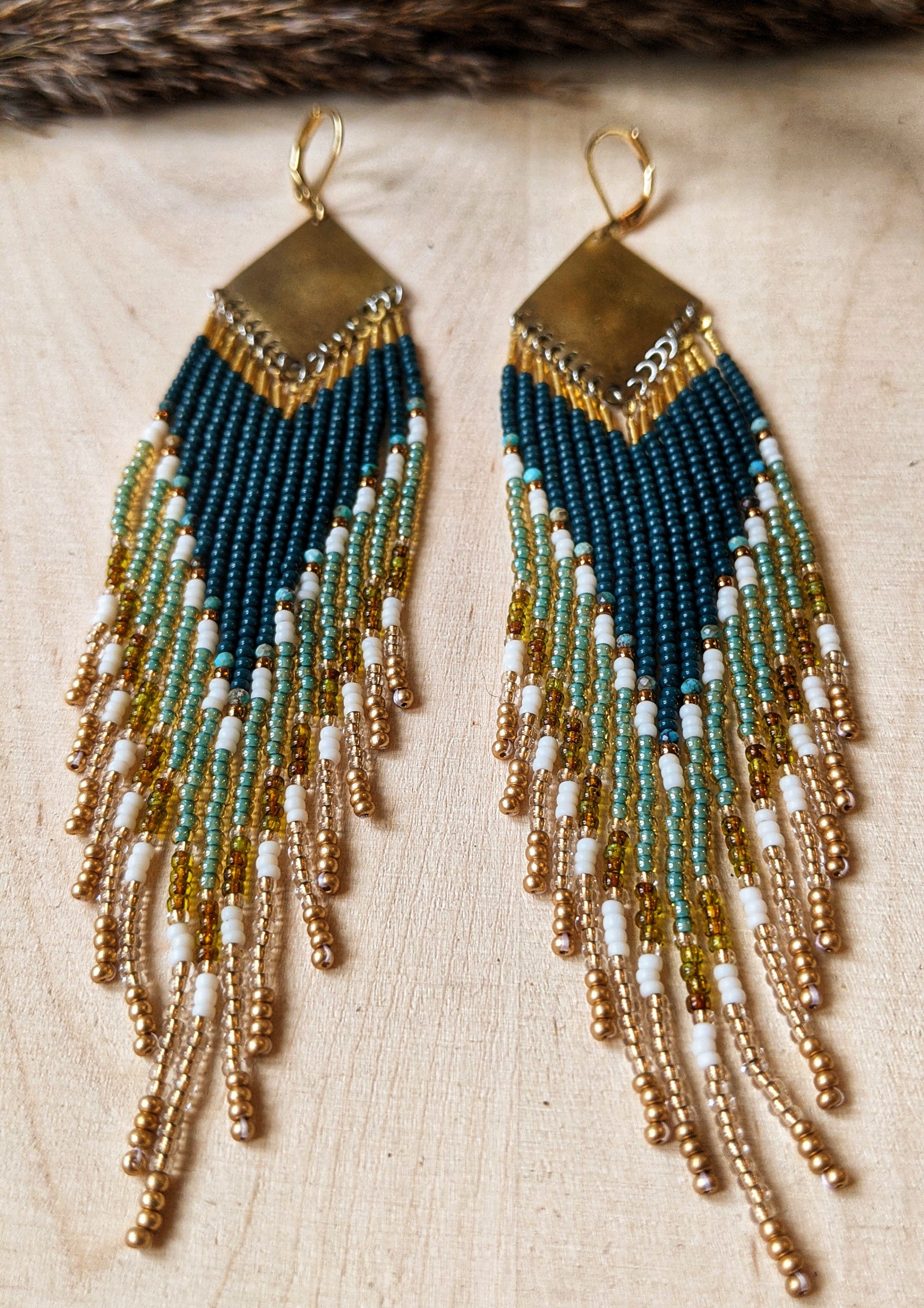 Close-up of  Moon & Milk handcrafted beaded earrings with dark green, gold, turquoise stones, cream glass beads, and brass accents.