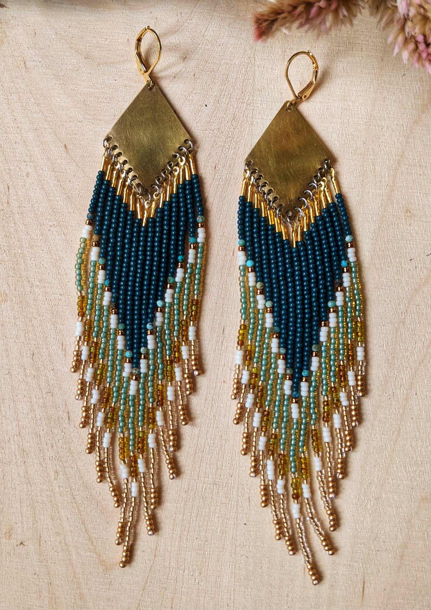 Close-up of  Moon & Milk handcrafted beaded earrings with dark green, gold, turquoise stones, cream glass beads, and brass accents.