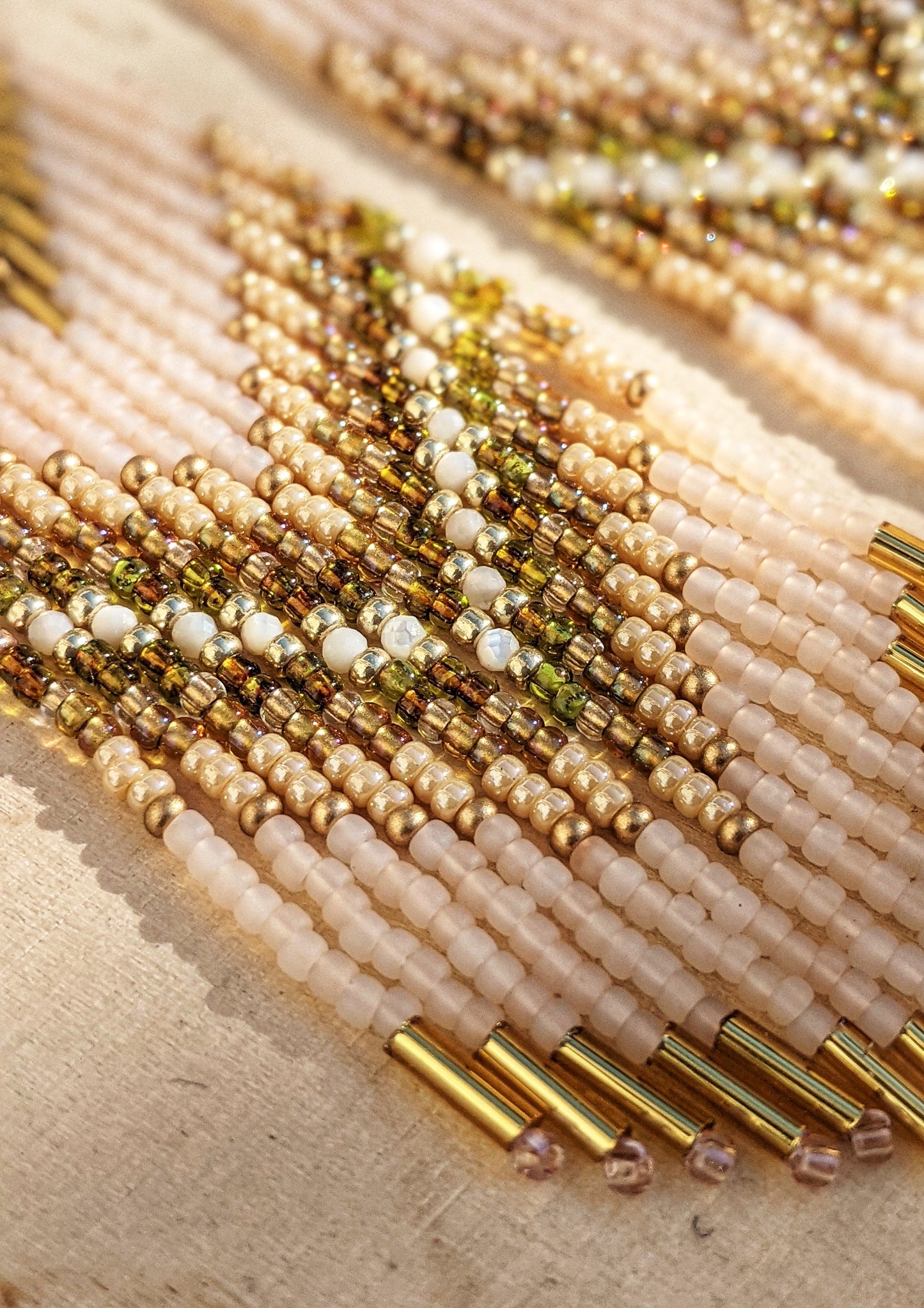 Moon & Milk handmade beaded earrings with cream, gold, olive, Mother of Pearl, and white beadwork in a chevron pattern, finished with brass findings and soft pink tips.