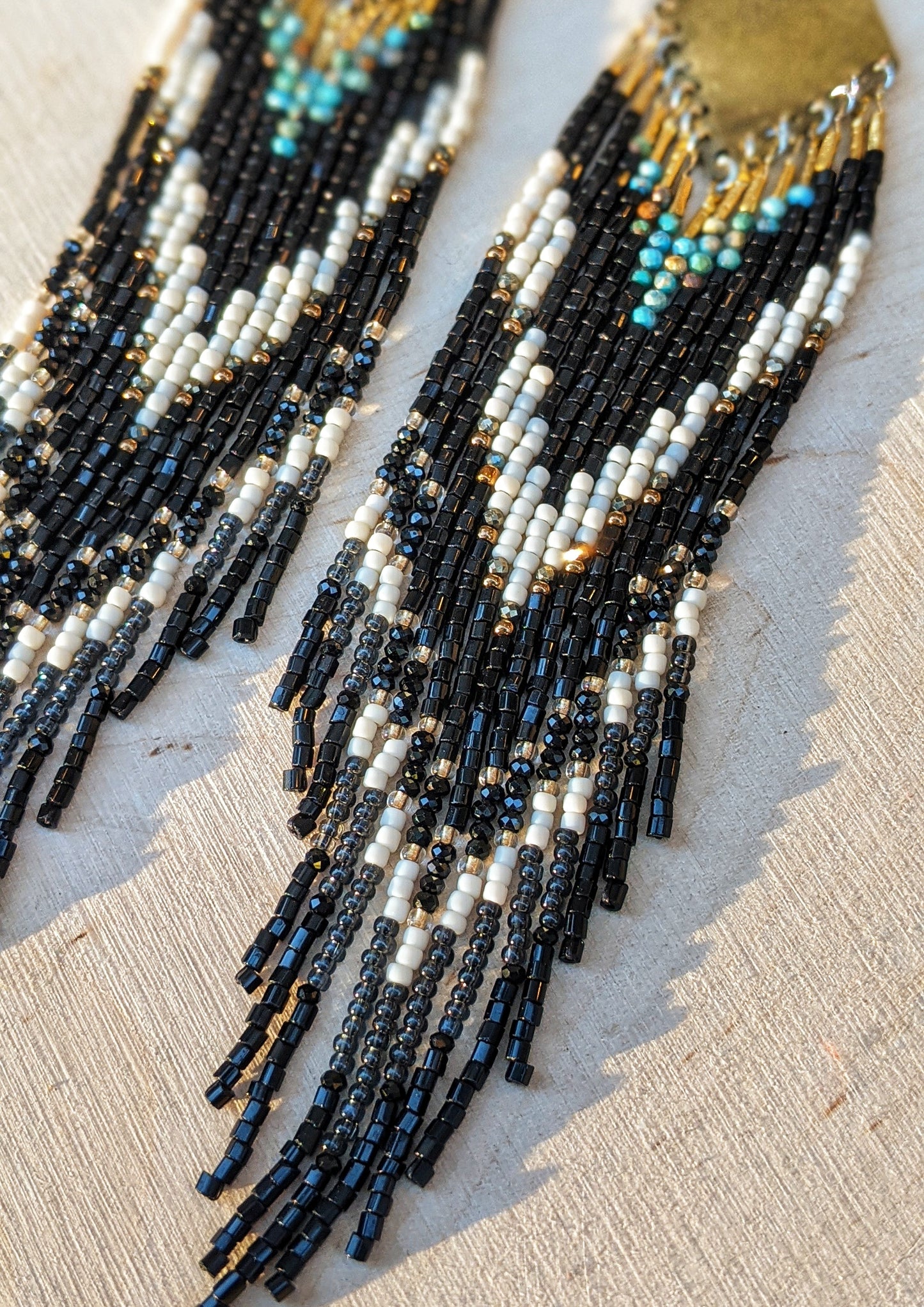 Long native beaded earrings in black, cream, and turquoise stones with brass tops, handcrafted for lovers of artisan jewelry and wearable art by Moon & Milk.