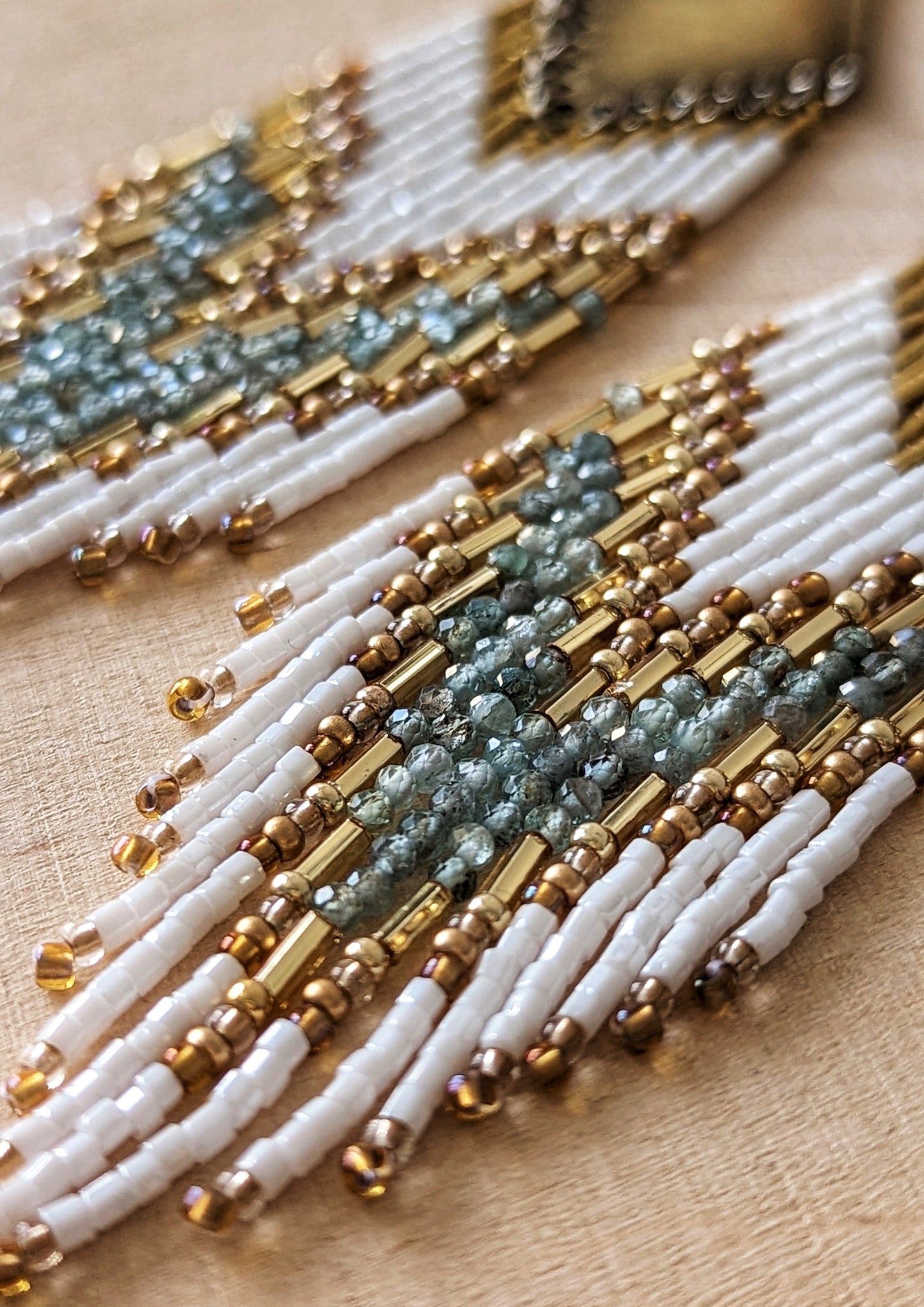 Elegant beaded earrings with white, gold, and soft aqua accents, displayed on a light wood background with delicate dried flowers nearby.- Moon & Milk
