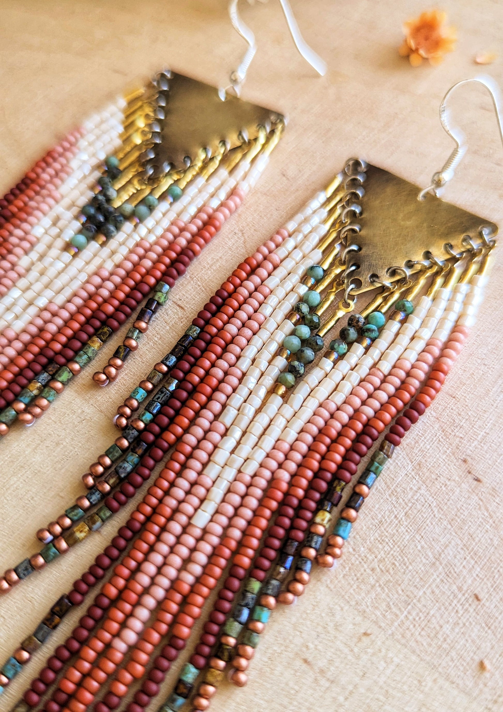 Moon & Milk beaded earrings featuring ivory, rust, pink, turquoise, and brown beaded fringes with brass triangle tops, inspired by wild desert blooms and earthy tones.