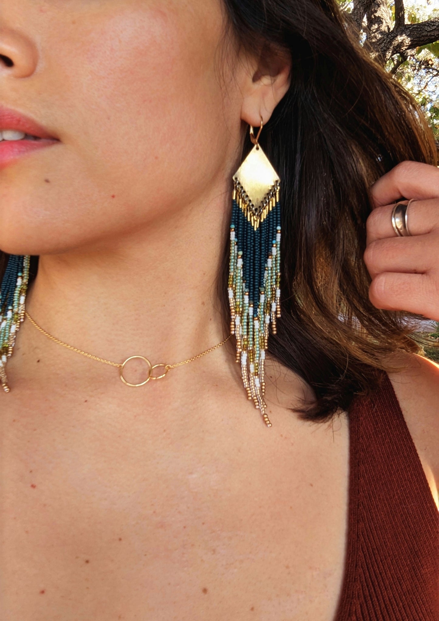 Close-up of a woman wearing Moon & Milk handcrafted beaded earrings with dark green, gold, and cream glass beads and brass accents, paired with a gold circle necklace.